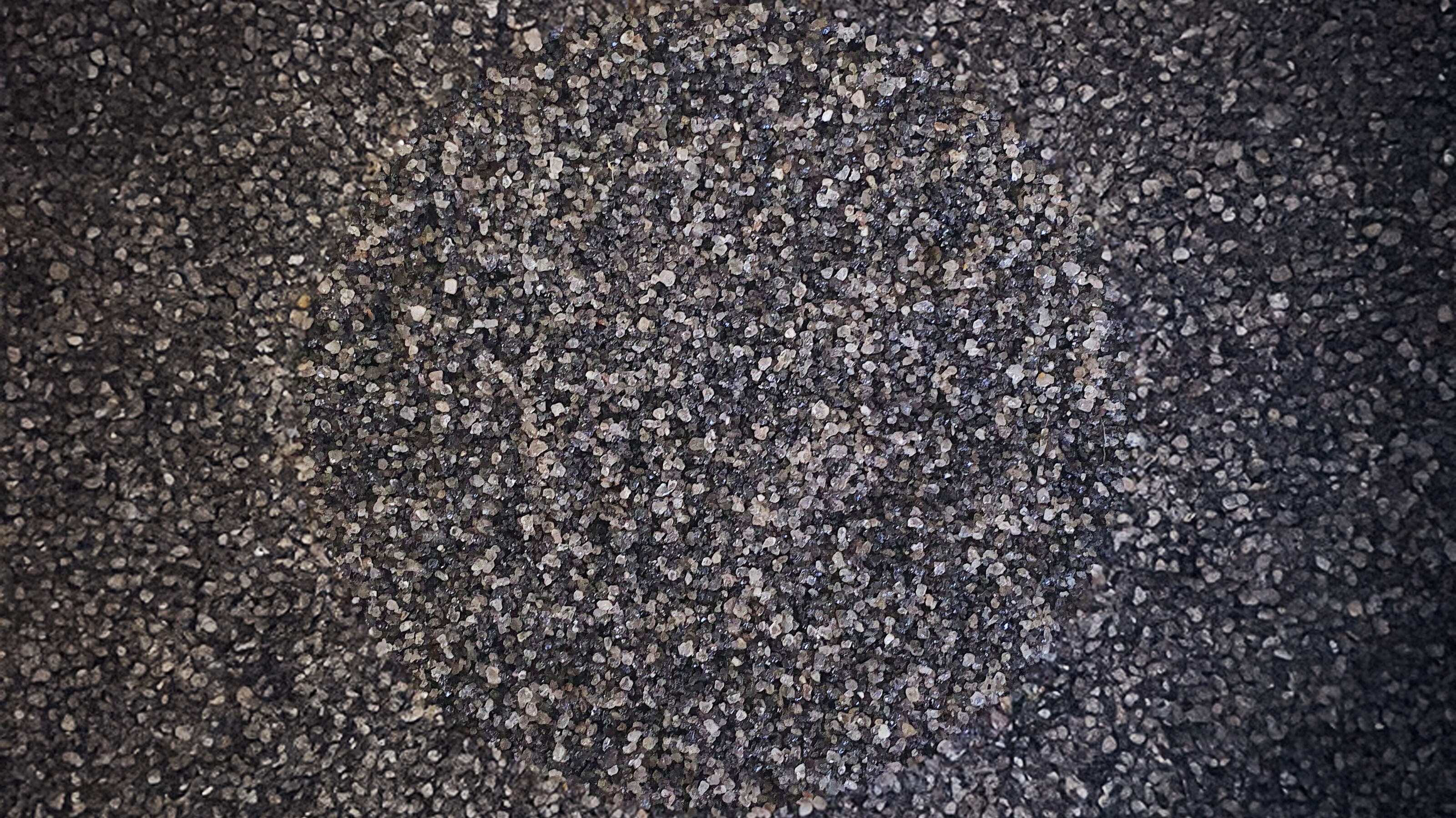 Donkere, korrelige textuur met grijze spikkels, als asfalt in close-up.