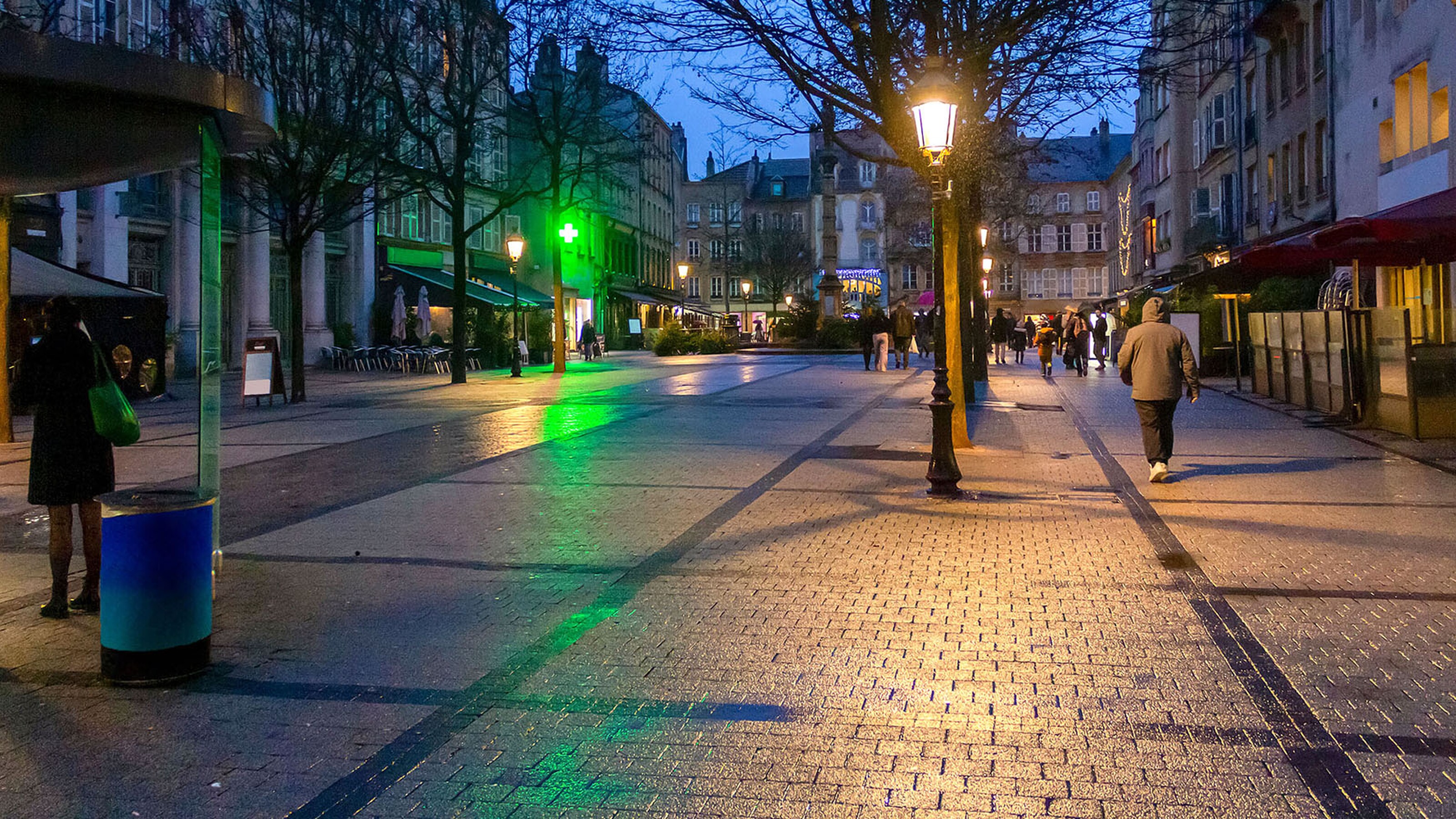 Avondzicht op natte, lege winkelstraat met straatlampen en twee wandelaars