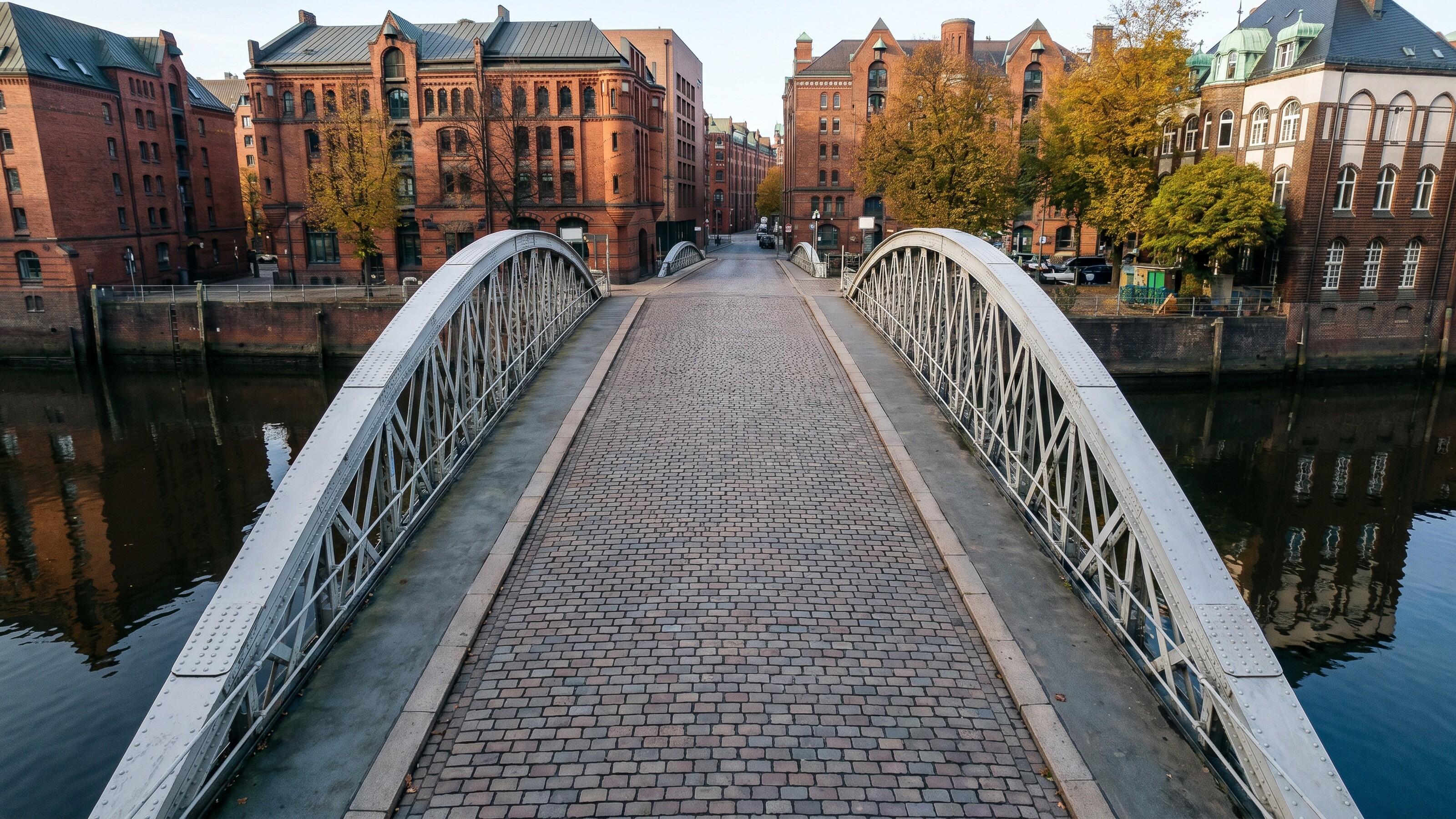 Witte boogbrug met kasseien over een gracht, bakstenen gebouwen op de achtergrond.