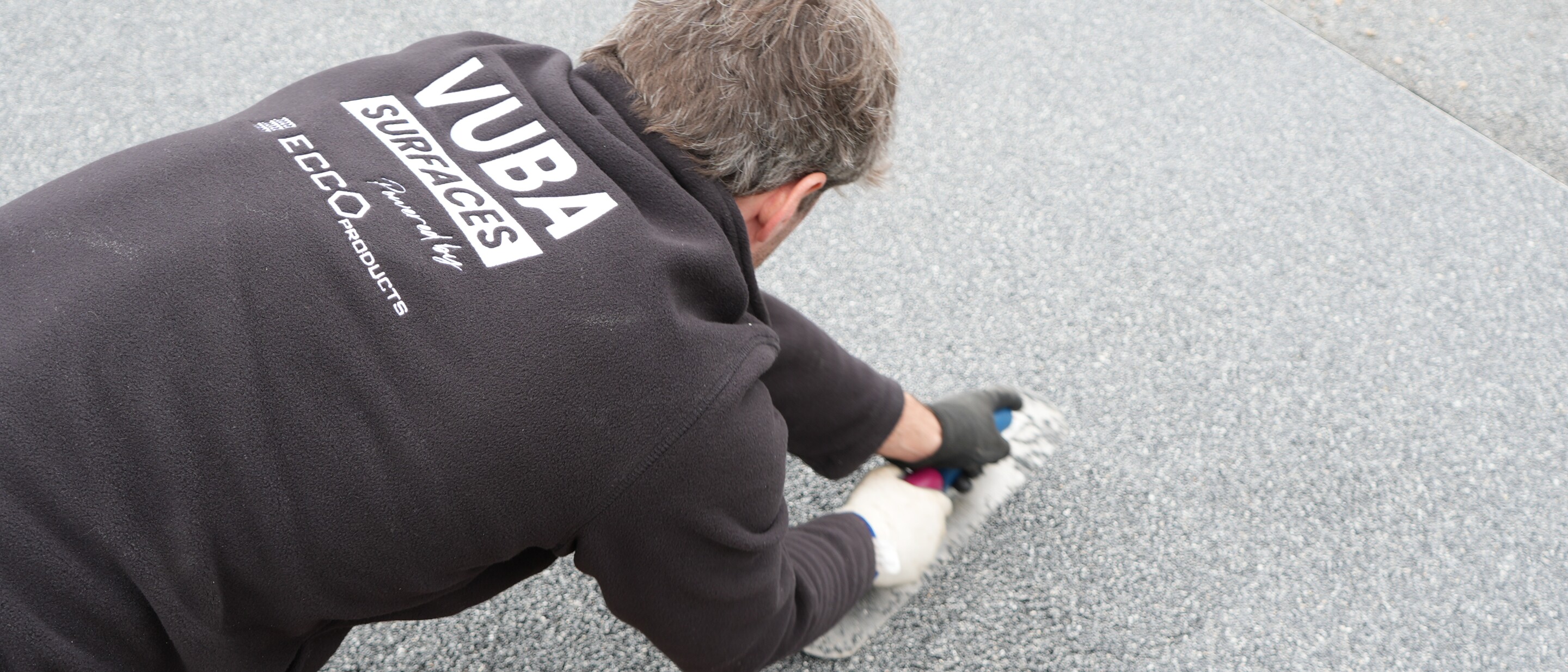 Man in black NUBA shirt kneeling and working on asphalt surface