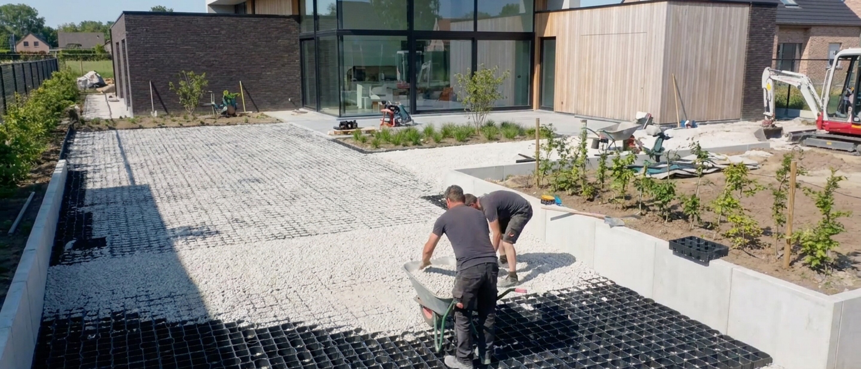 Worker kneeling on gravel, installing black ground grid outside a modern house