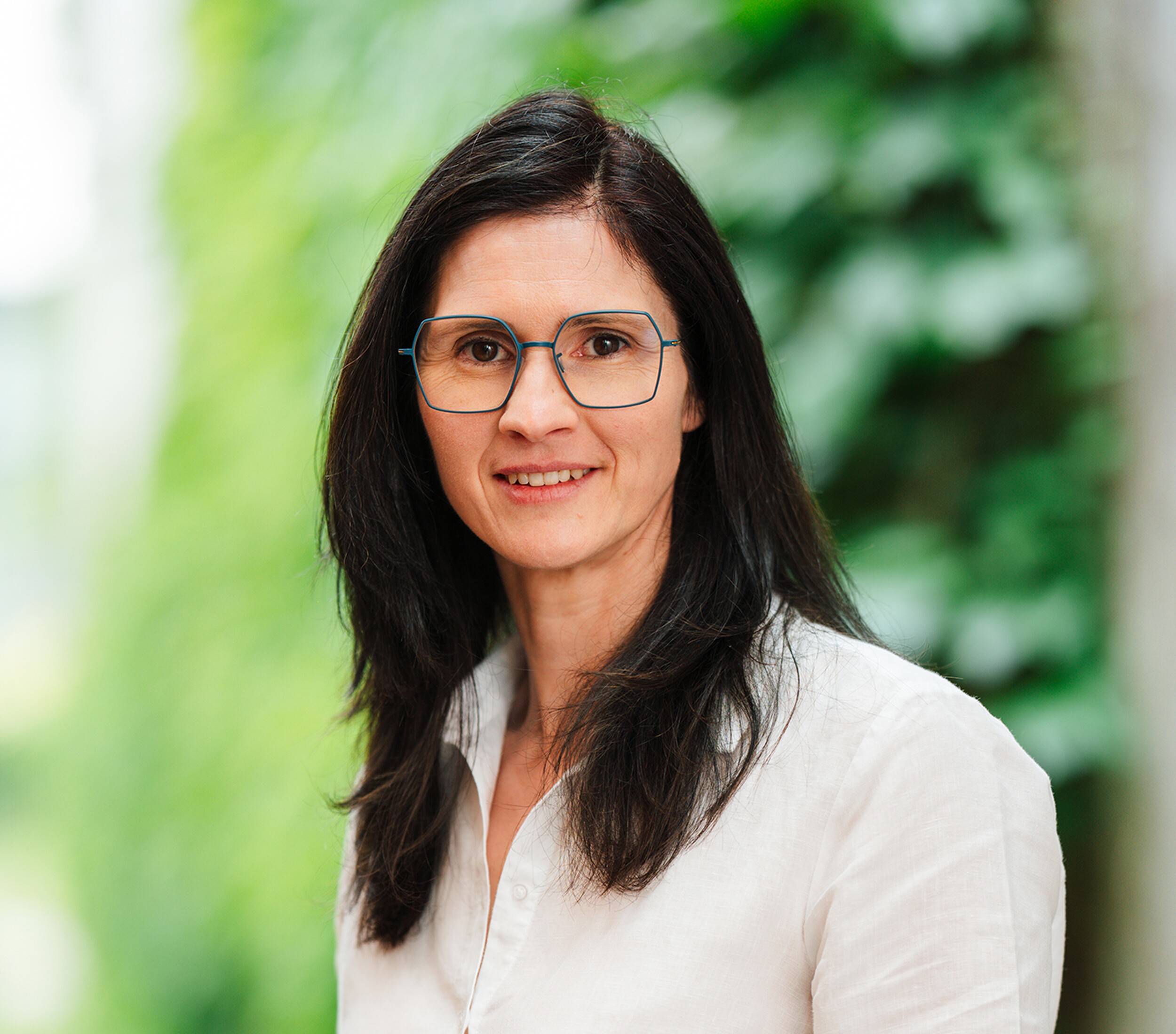 Portretfoto van een glimlachende vrouw met bril en donker haar, groene achtergrond