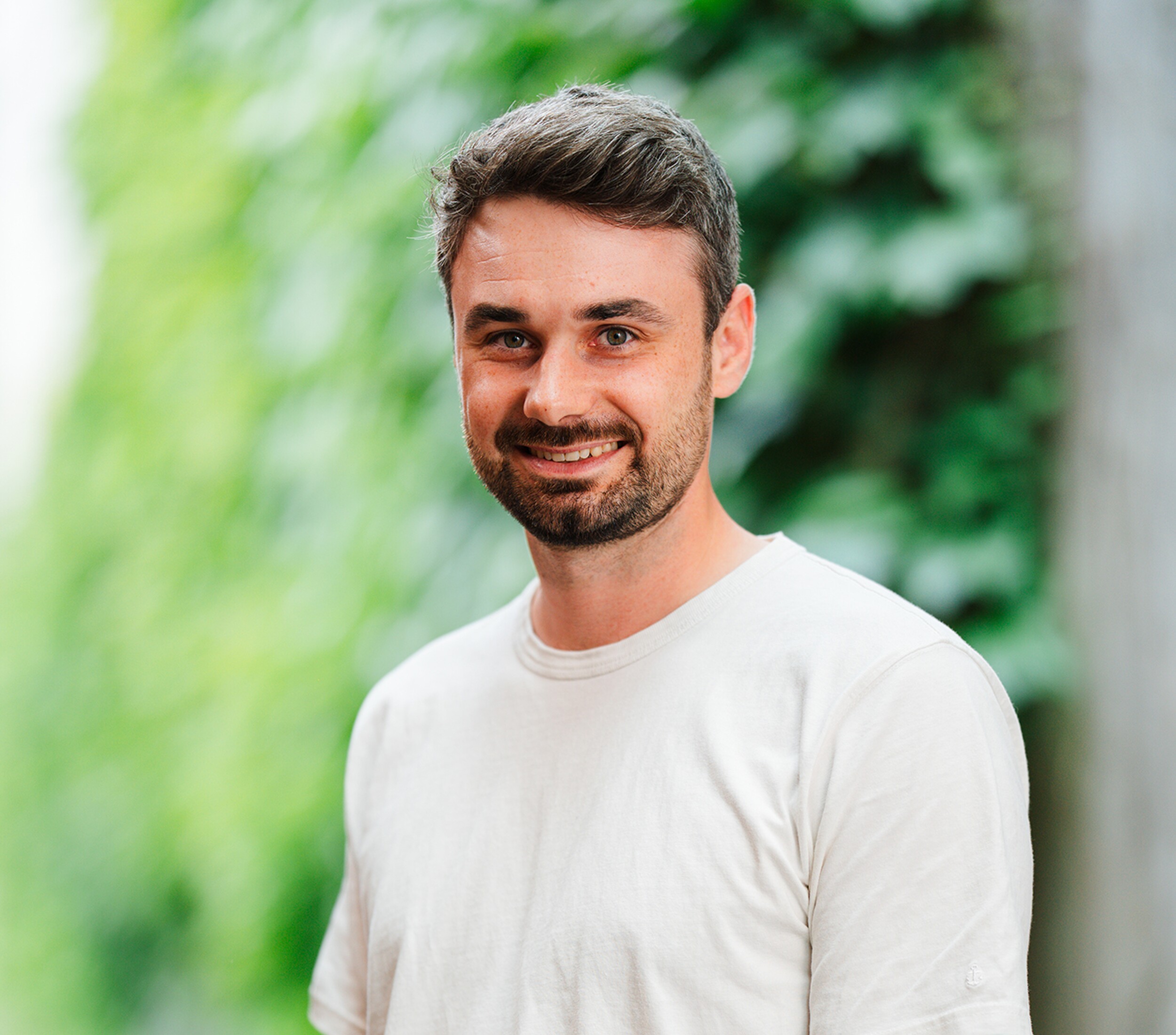 Portretfoto van een glimlachende man in wit T-shirt, groene achtergrond.