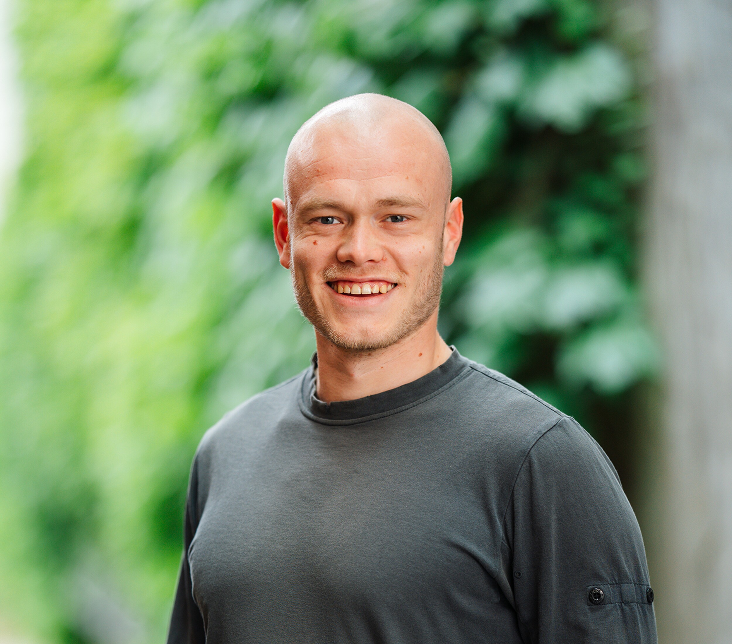 Lachende kale man in donker T-shirt, onscherpe groene achtergrond.