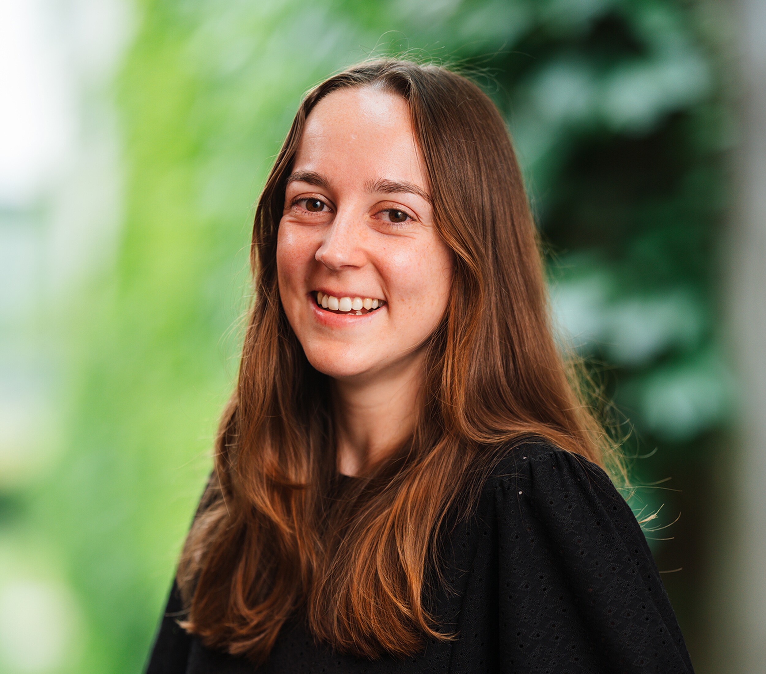 Portretfoto van lachende vrouw met lang bruin haar tegen groene achtergrond