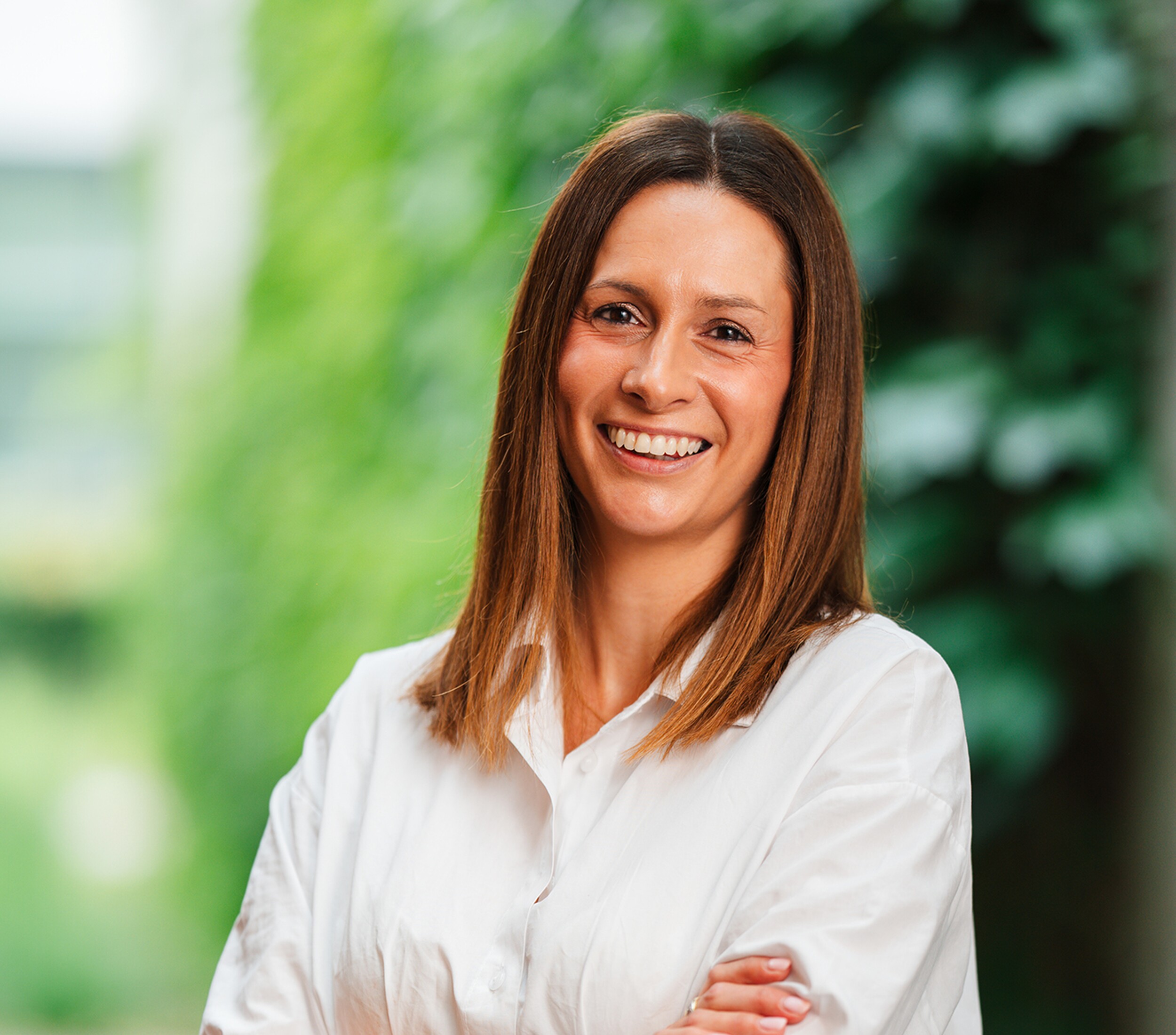 Lachende vrouw in witte blouse met gekruiste armen, groene achtergrond.