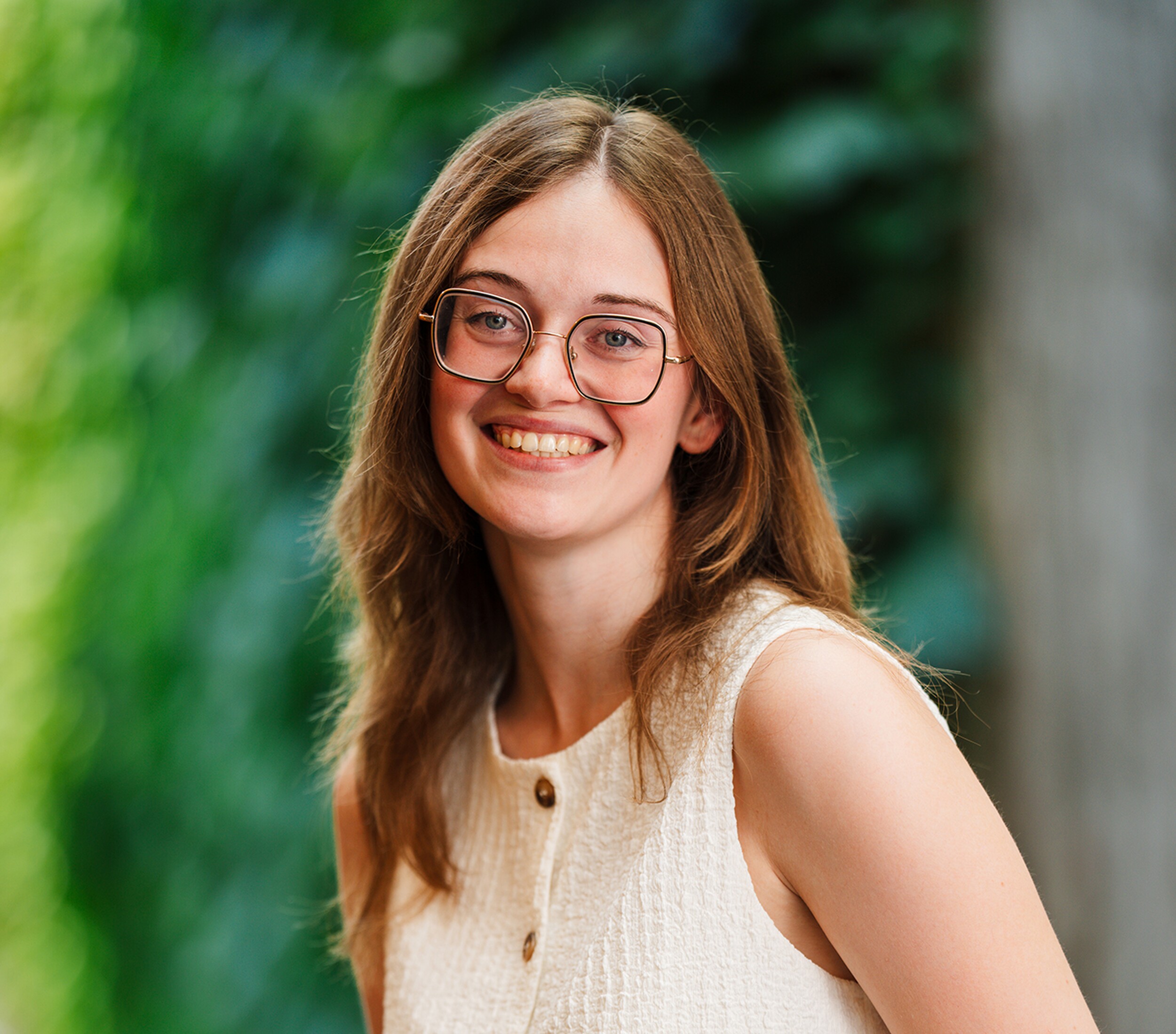 Glimlachende jonge vrouw met bril, in witte top, tegen groene achtergrond.