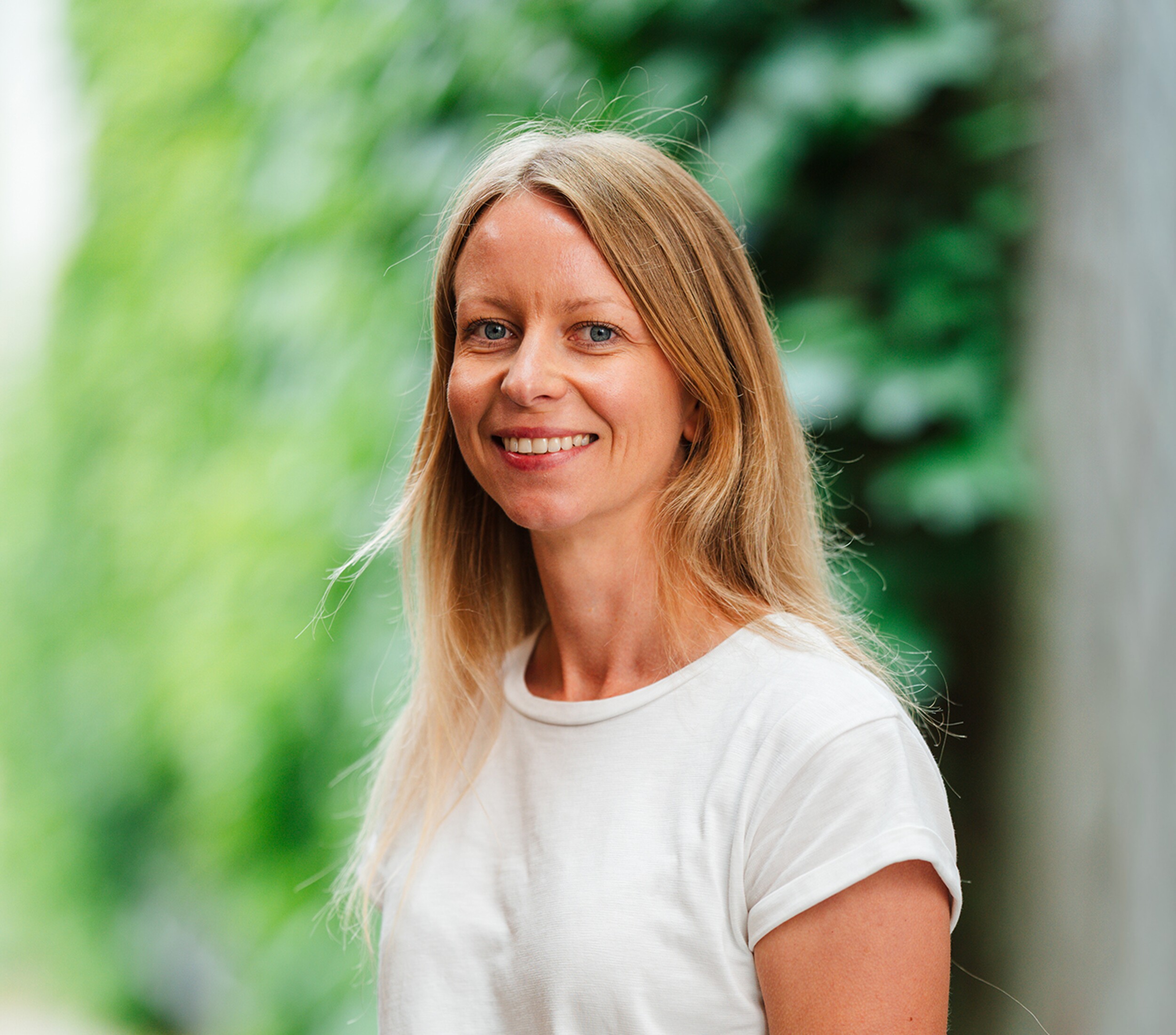 Lachende vrouw met lang blond haar in witte T-shirt, buiten met groene achtergrond