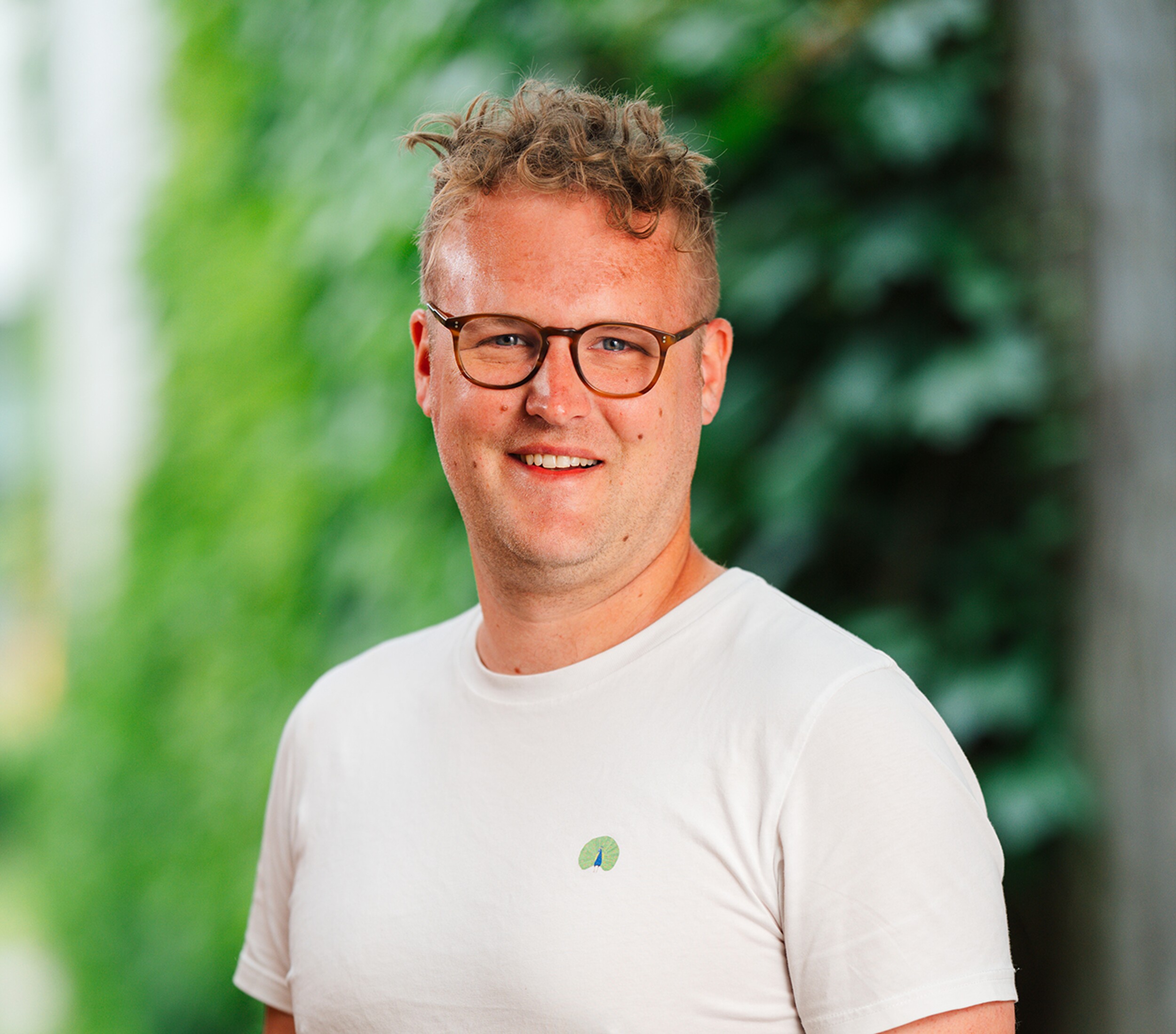 Portretfoto van een glimlachende man met bril in wit T-shirt buiten.