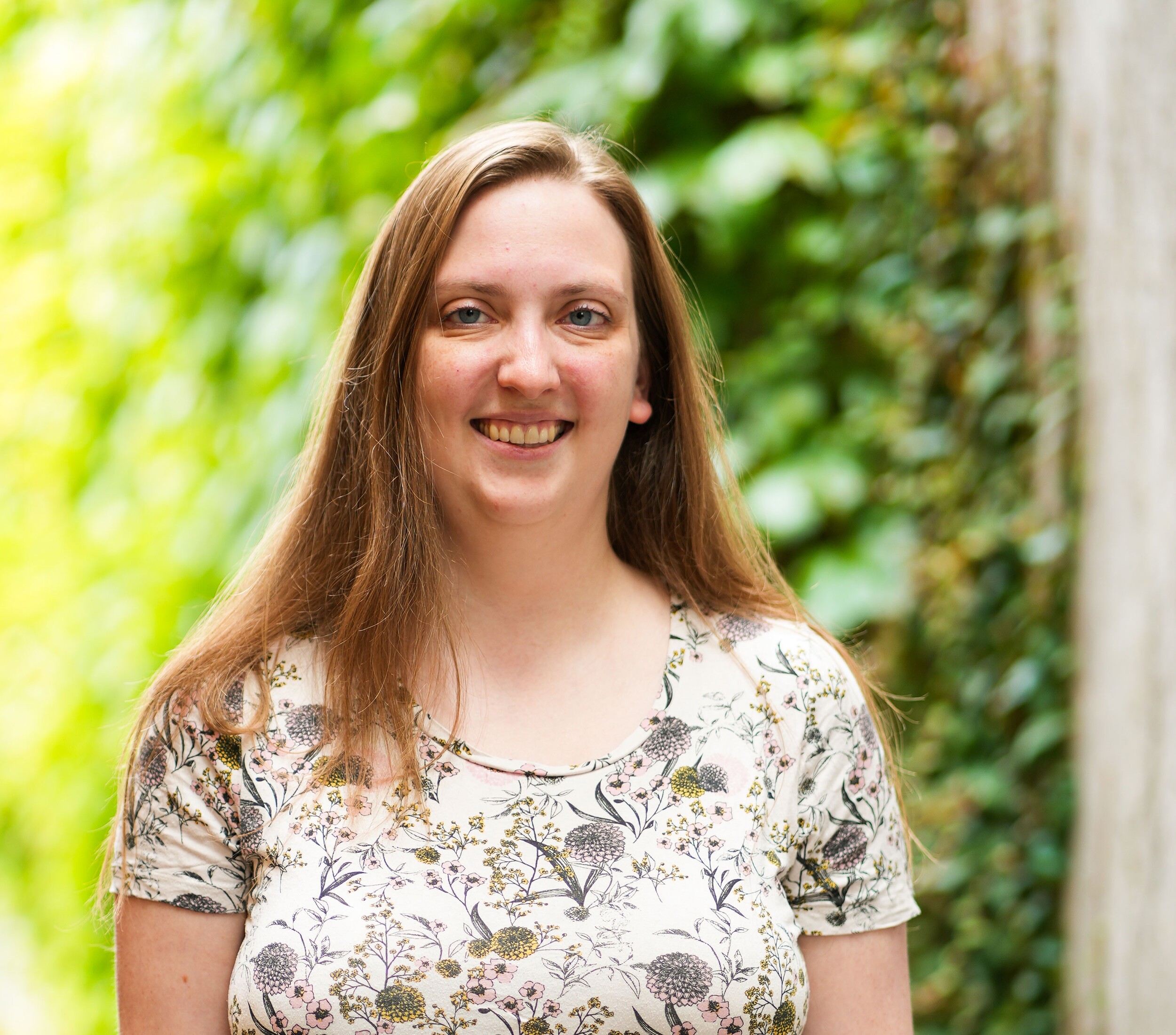 Smiling woman in a floral top outdoors beside greenery