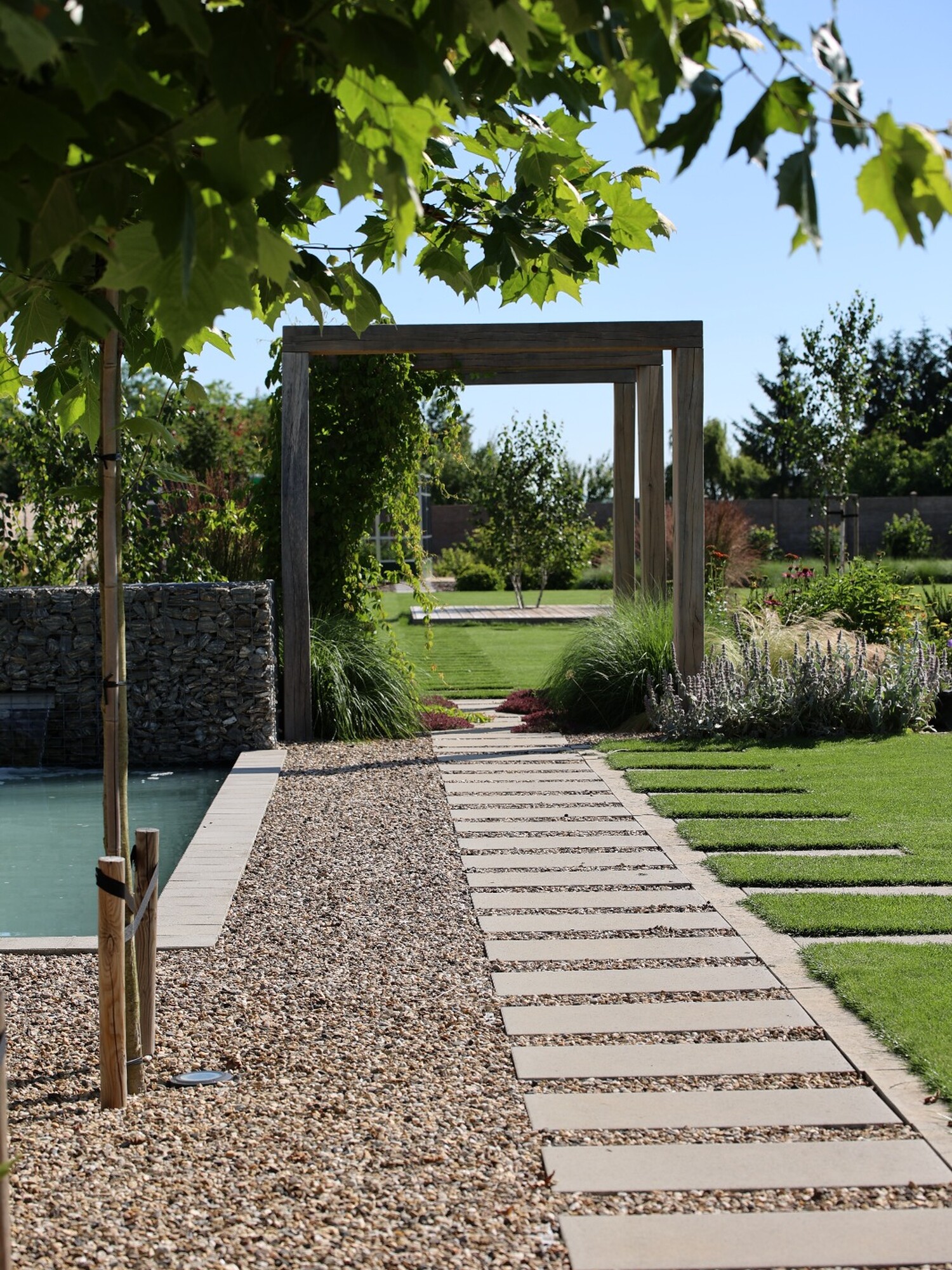 Allée en pierre à travers le jardin avec une pelouse tondue et des arbres feuillus sous un ciel bleu