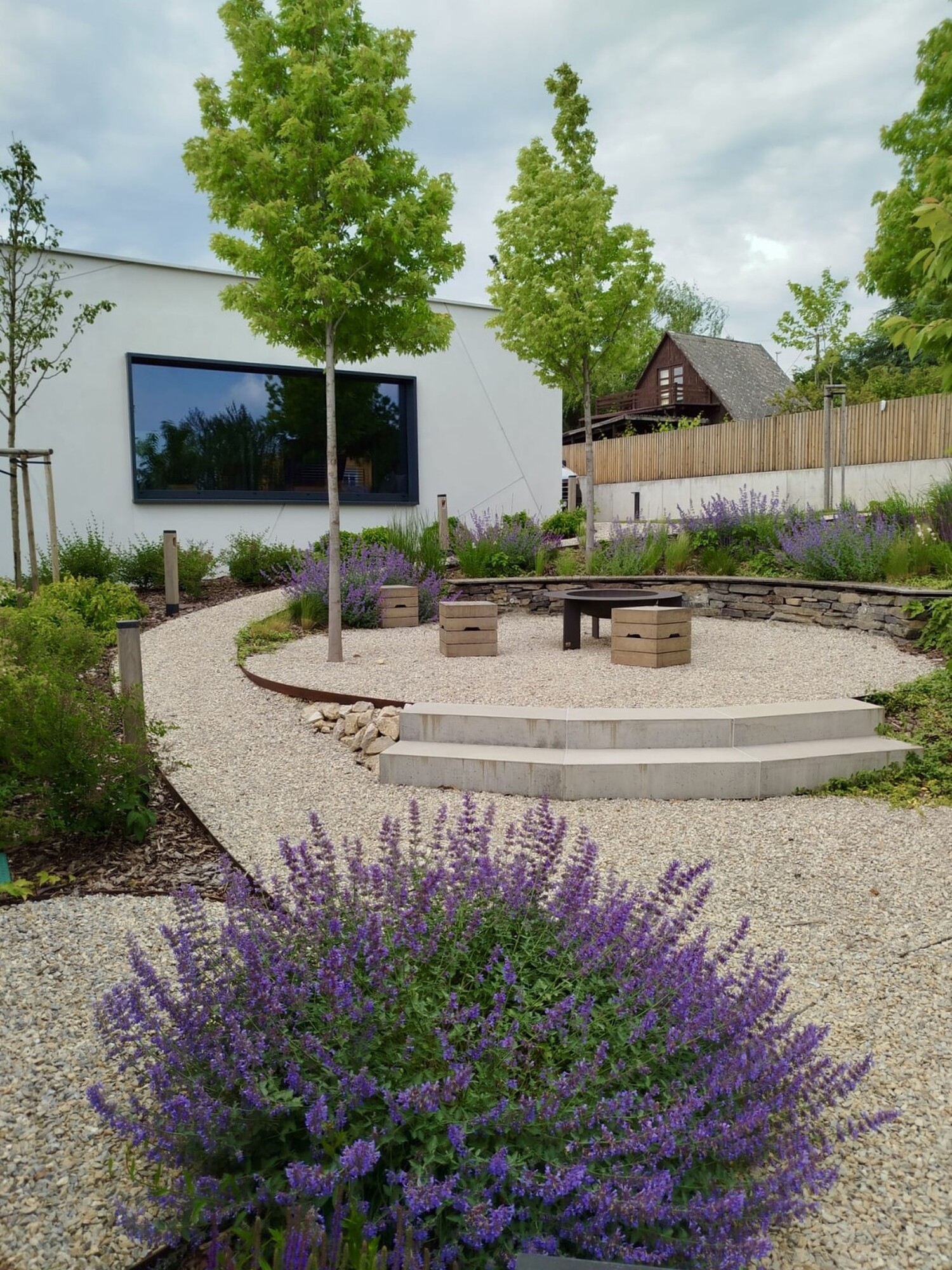 Cour intérieure de bureaux moderne avec chemin de gravier sinueux, bancs et fleurs violettes