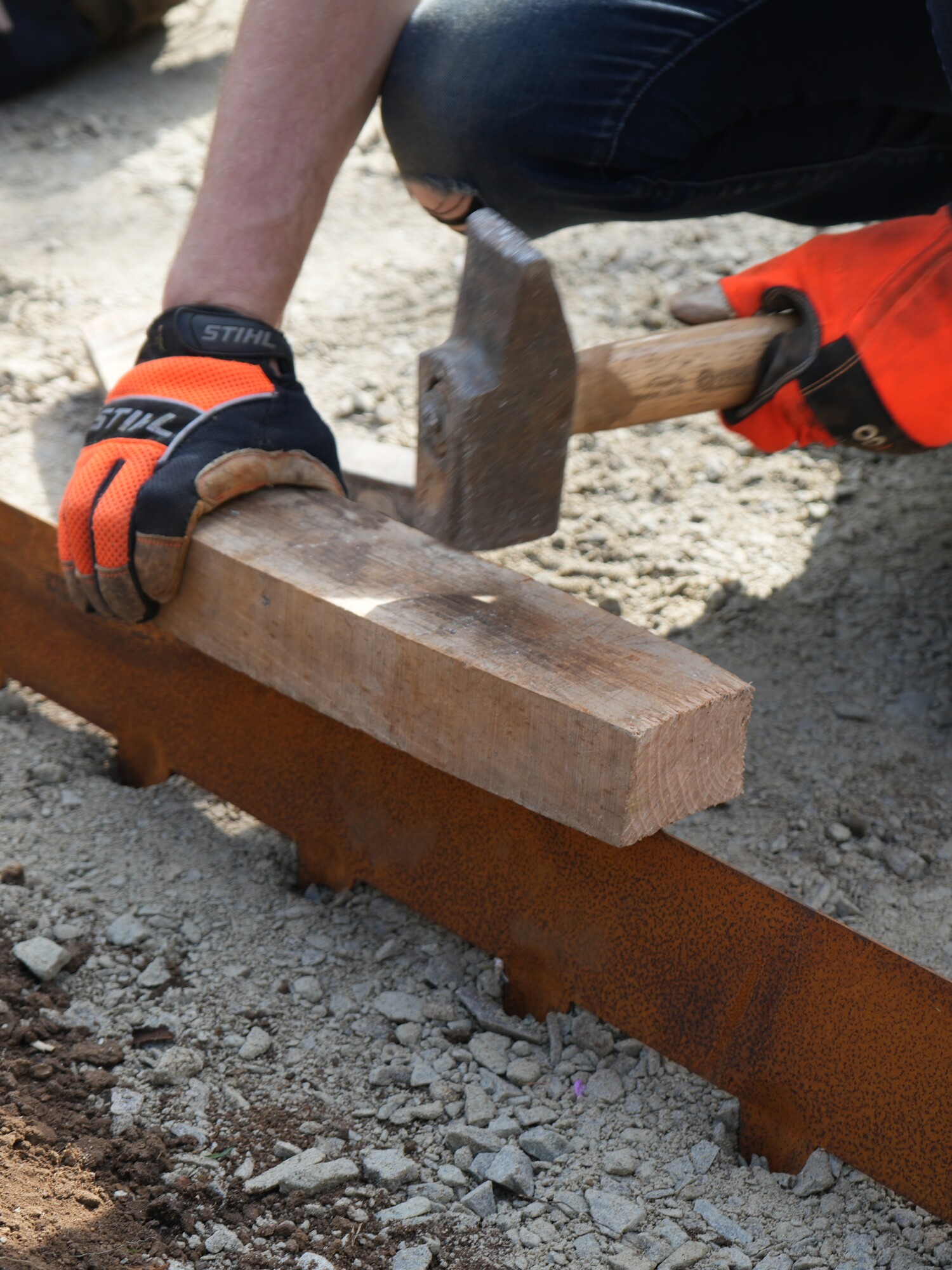 Personne portant des gants martelant un panneau de coffrage en bois sur un chantier de construction