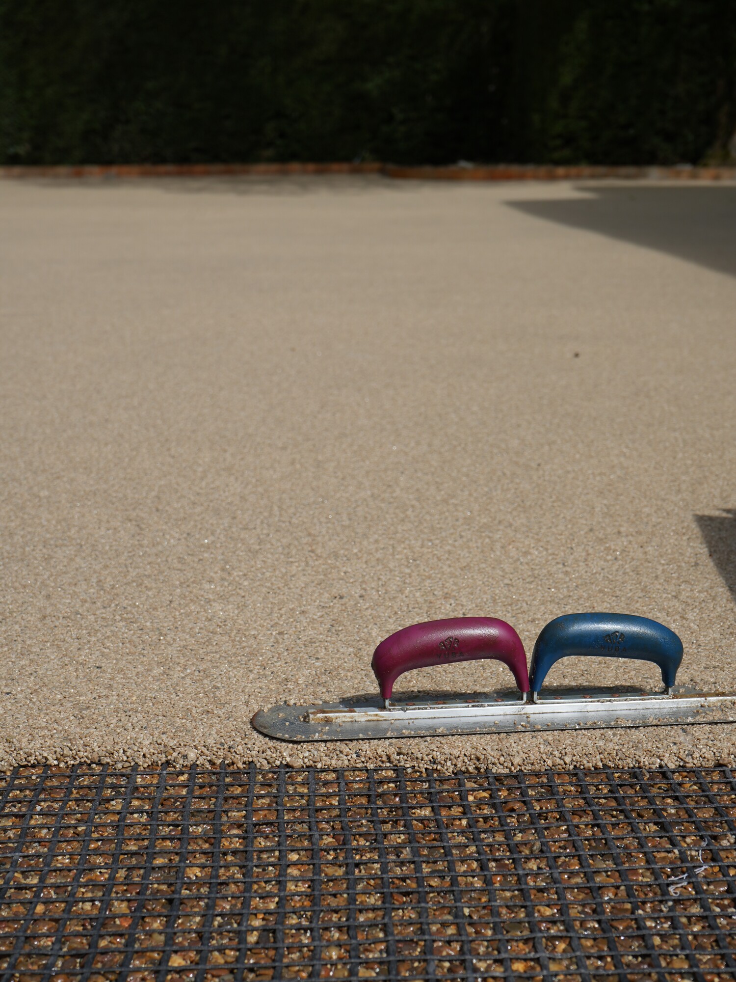 Two small U-shaped handles, pink and blue, on a curb beside textured pavement
