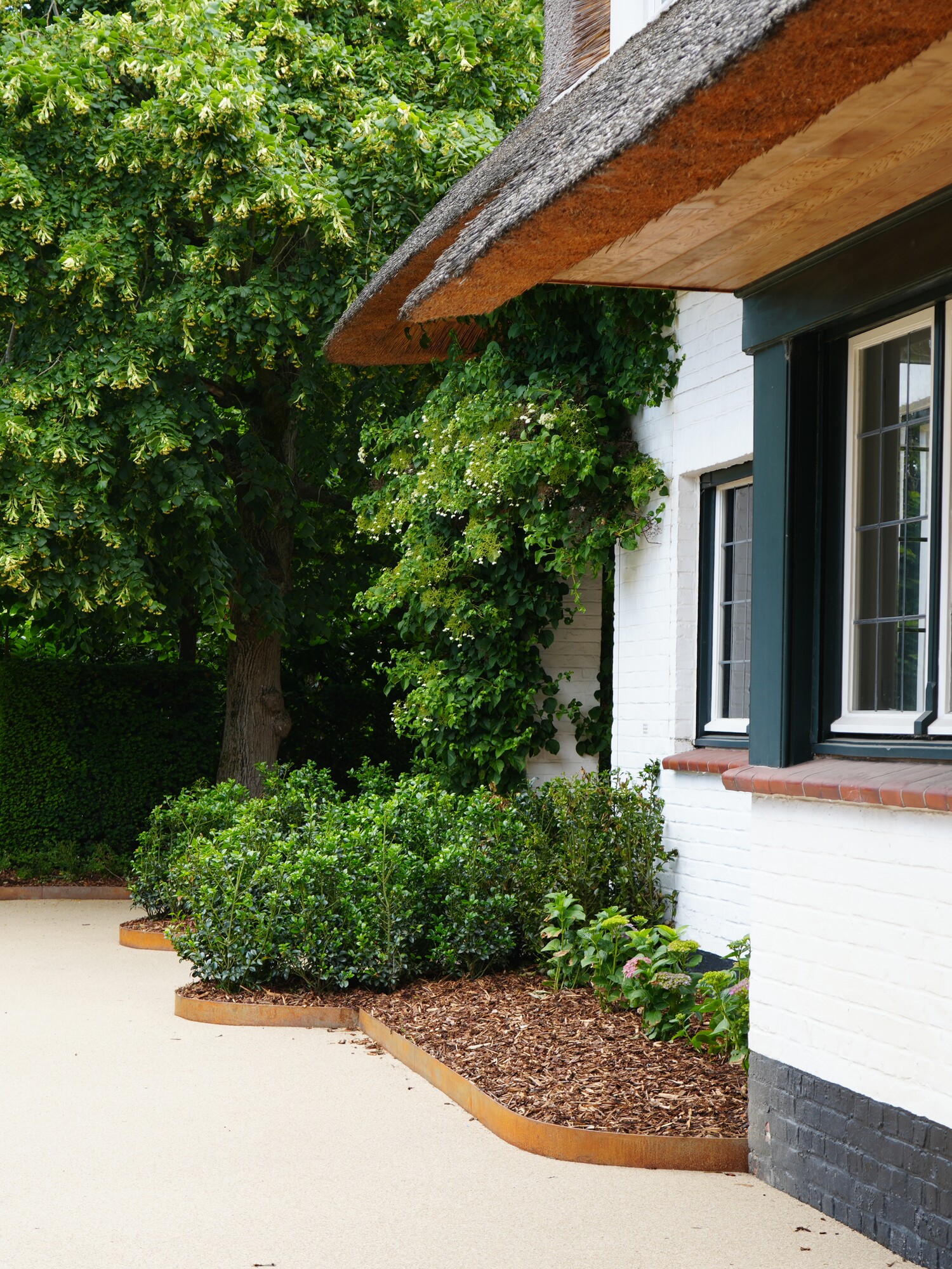 White house with black-framed windows beside a driveway and green trees