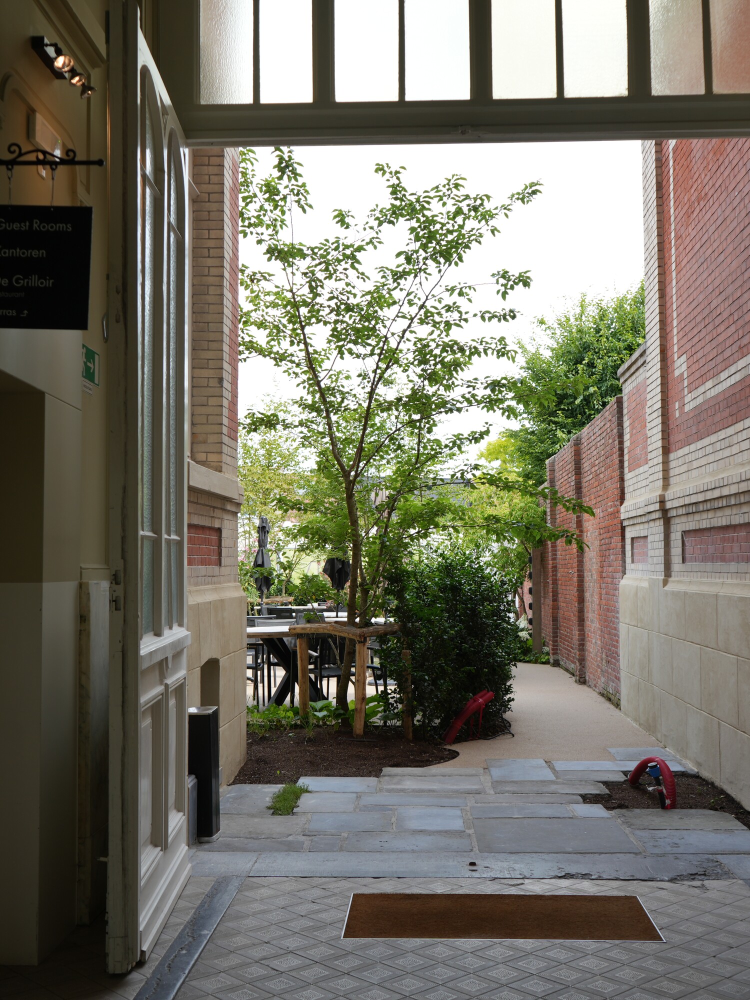 Passageway with mats, an open gate, and green plants at the end.