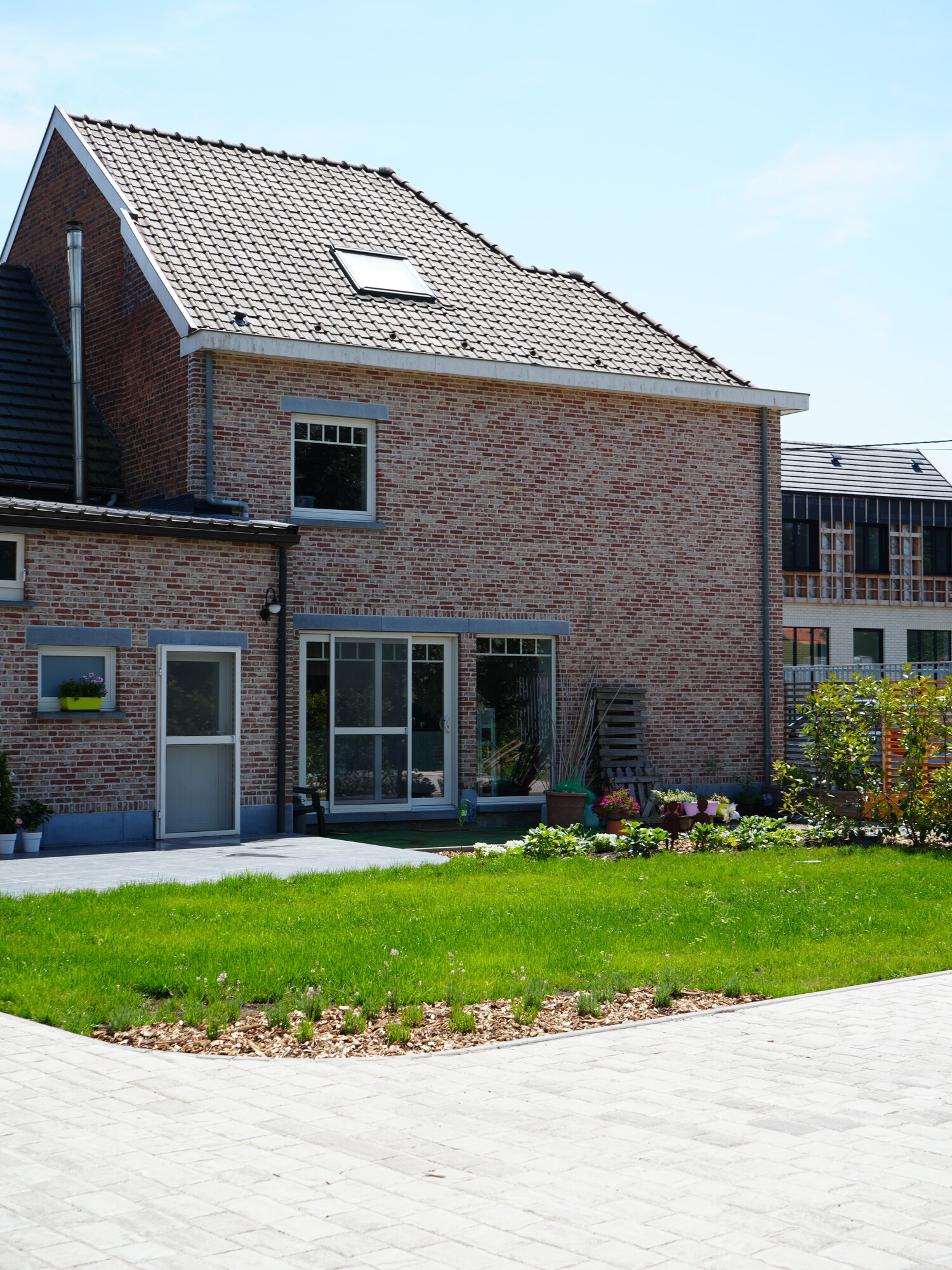 Two-storey brick house with solar panels, patio doors, and a sunny green lawn