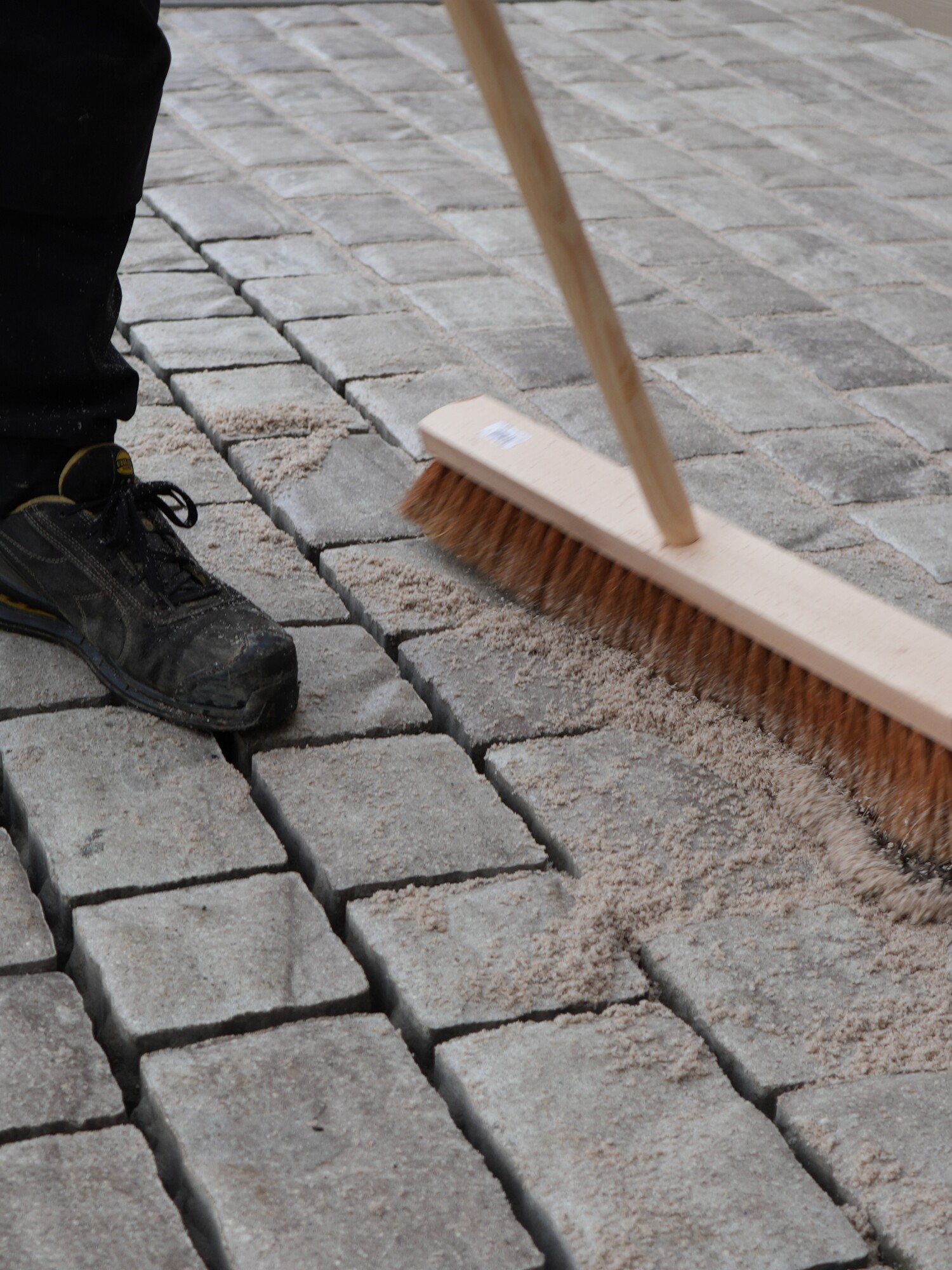Person sweeping a cobblestone sidewalk with a push broom
