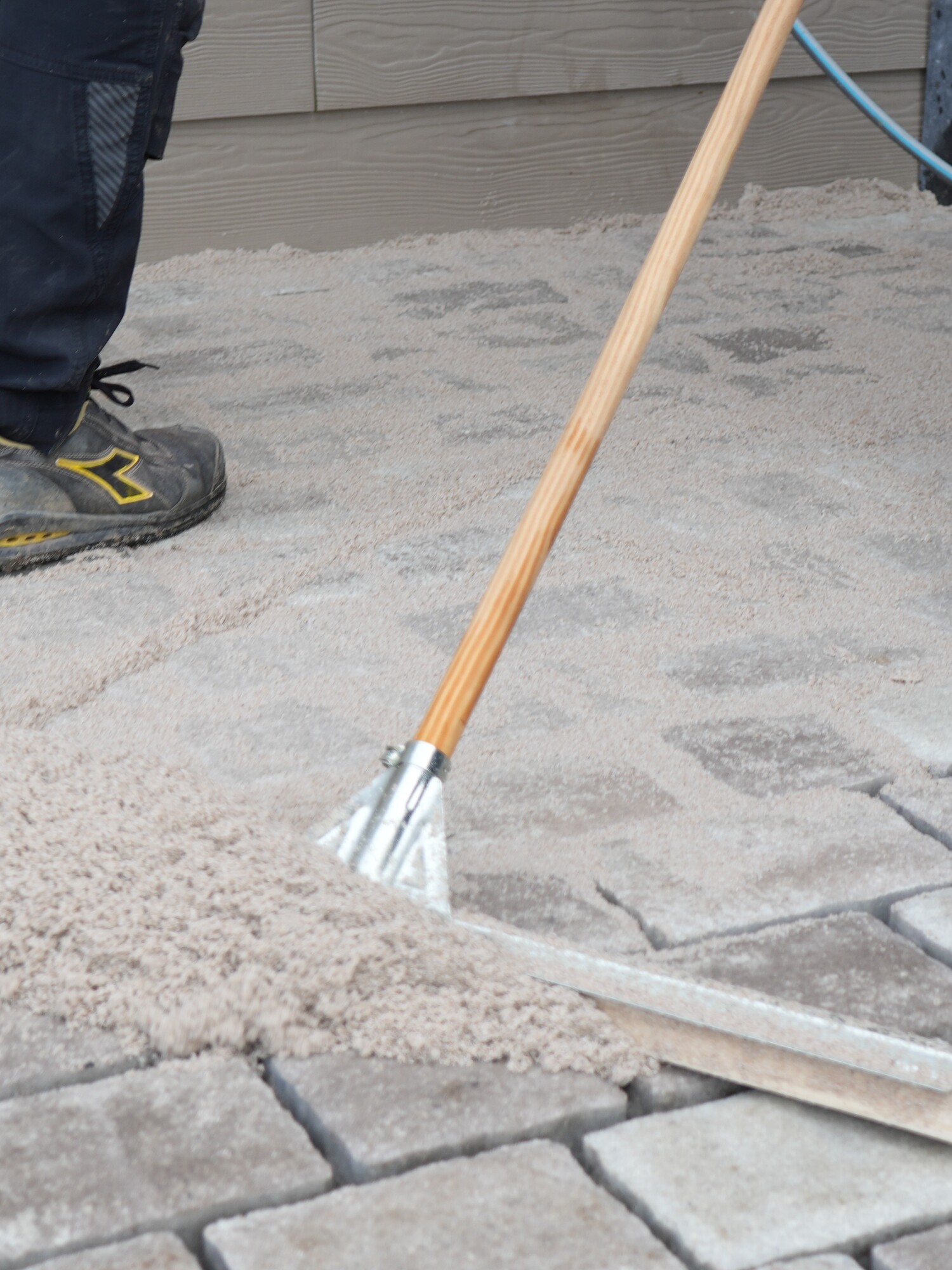 Workers leveling paving stones with a rake on a sidewalk