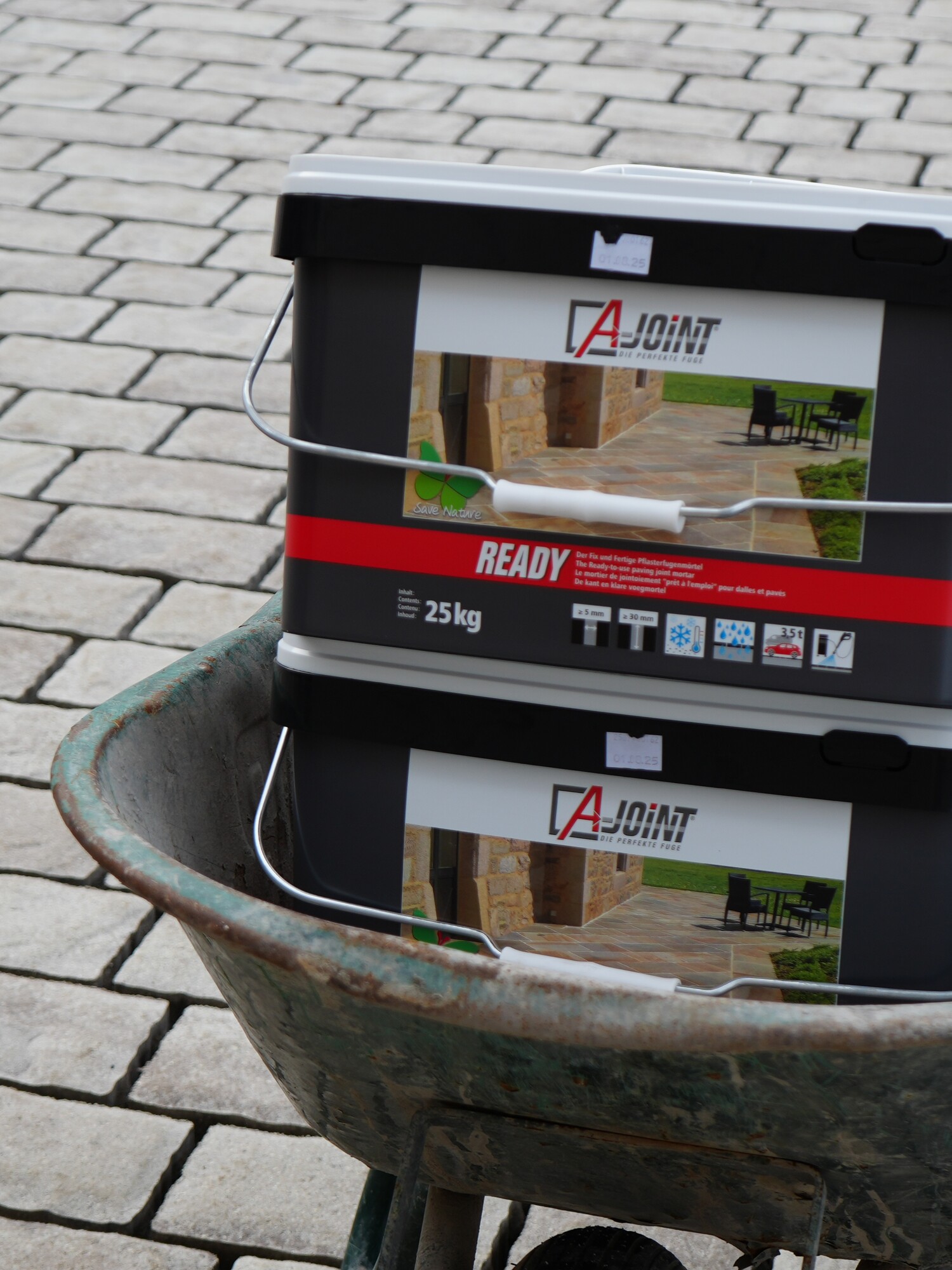 Wheelbarrow carrying two black paint buckets on a brick driveway