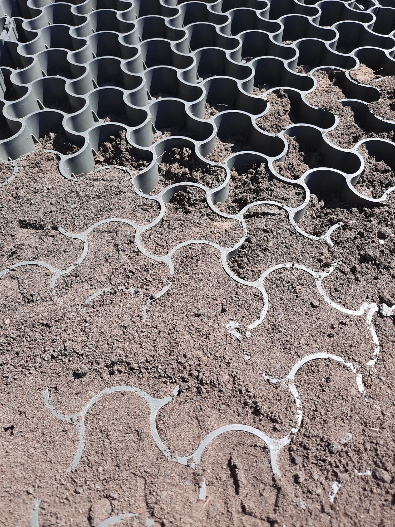 Wavy gray interlocking pavers laid over brown dirt on a sloped surface