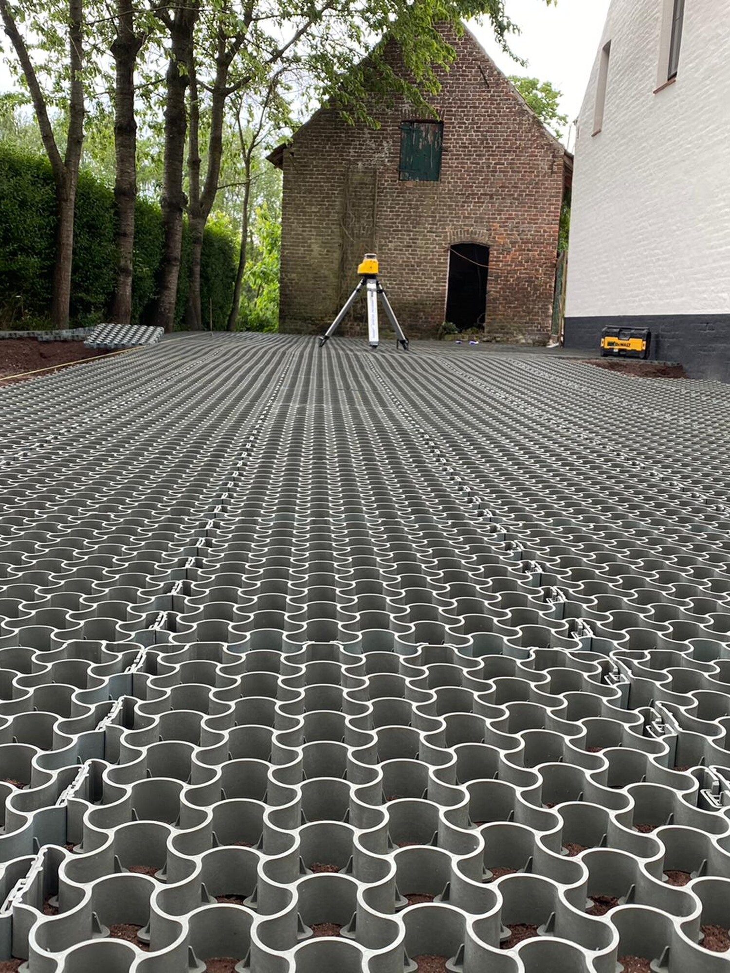 Interlocking grey pavers laid beside a white building and brick structure under trees