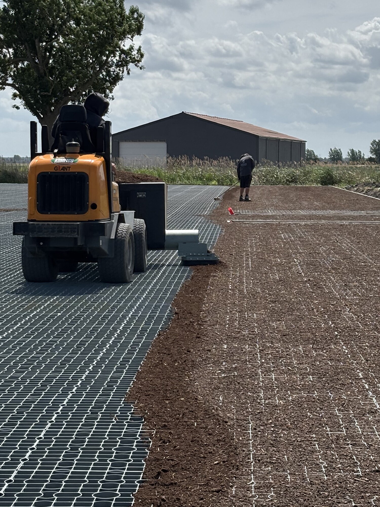Werker op tractor legt geogrid op bouwplaats onder bewolkte lucht
