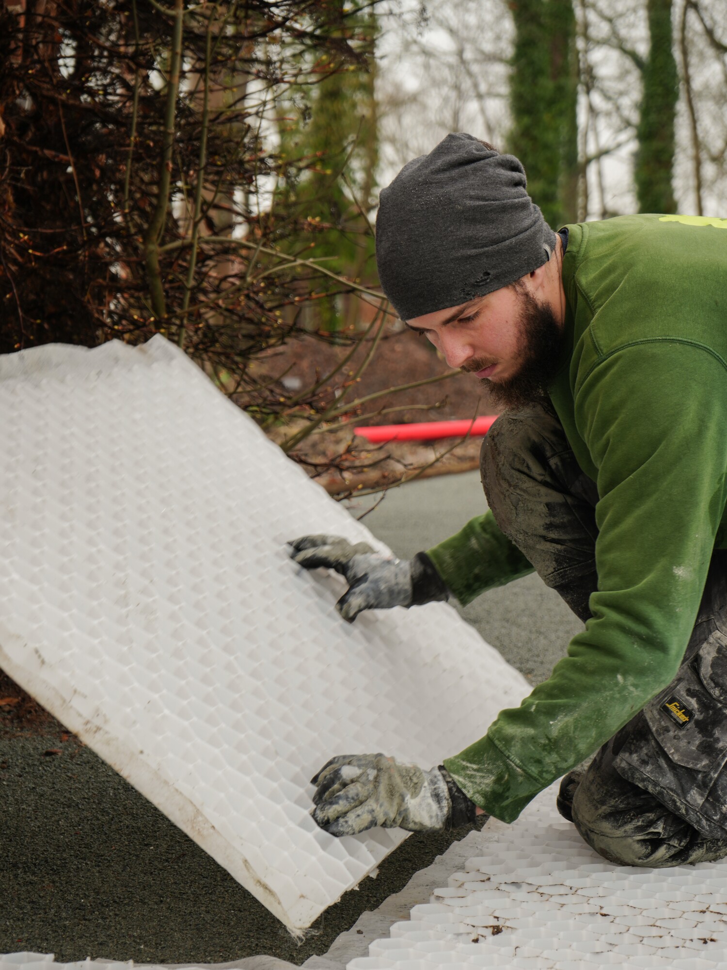 Man in green jacket installing white floor underlayment outdoors in winter