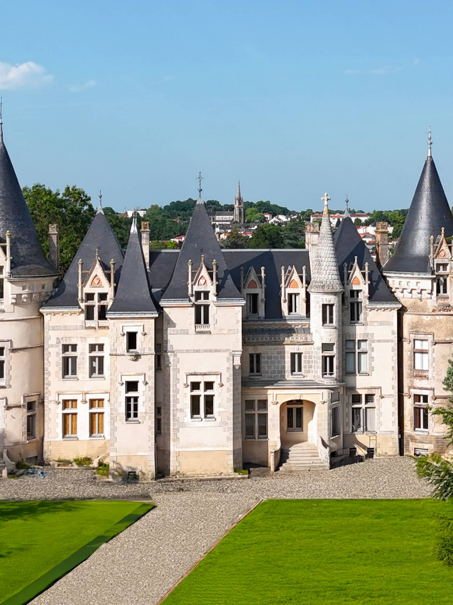 Vue aérienne d’un château blanc avec des tourelles au milieu de pelouses verdoyantes et d’arbres sous un ciel bleu