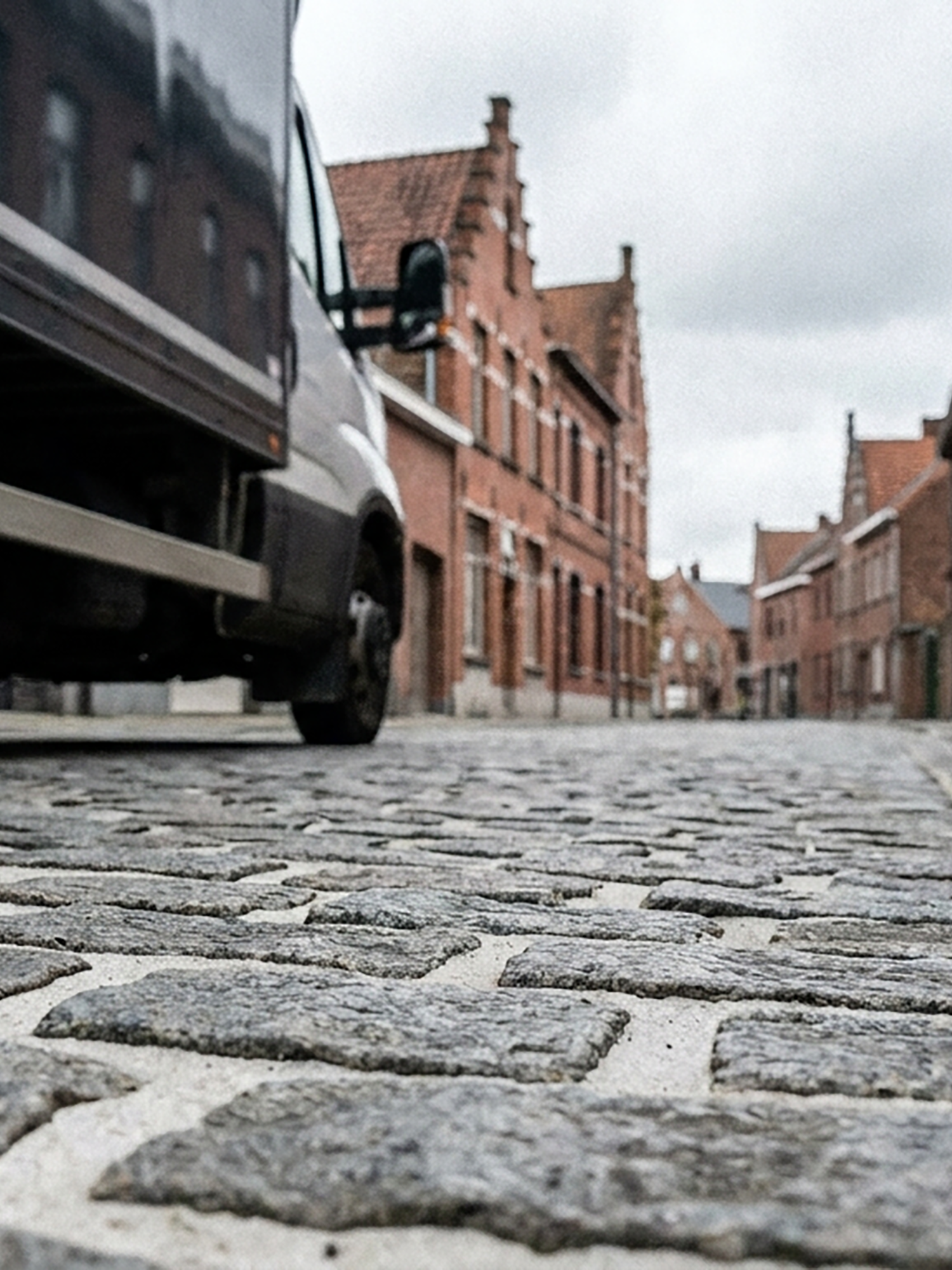 Low-angle view of a cobblestone street with brick buildings and a parked car