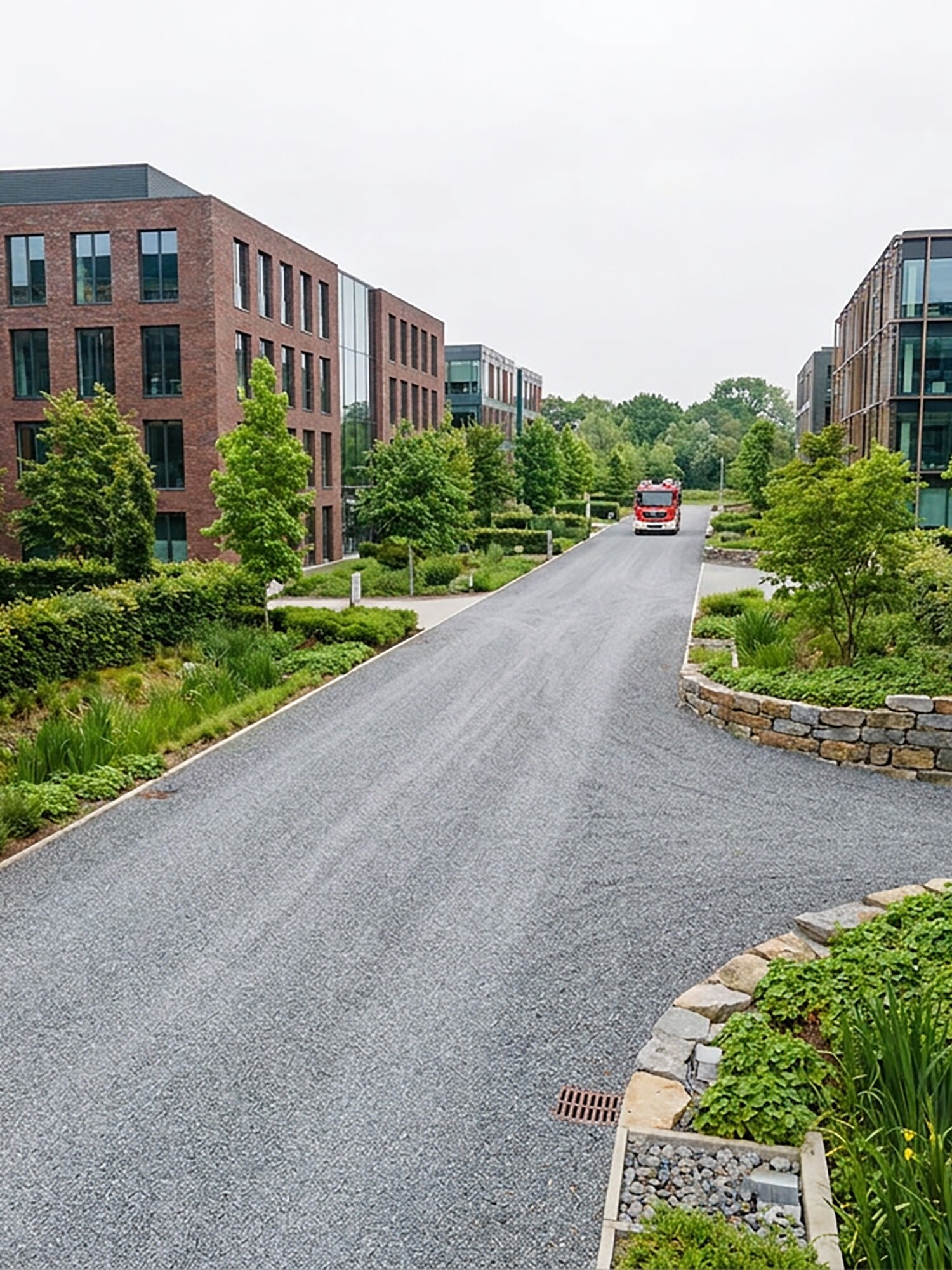 Curved paved path between brick buildings with greenery and a red car in the distance