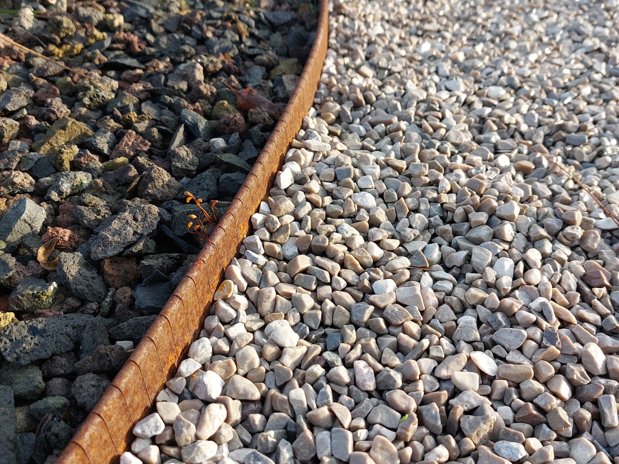 Curved gravel path bordered by rusted metal edging in sunlight