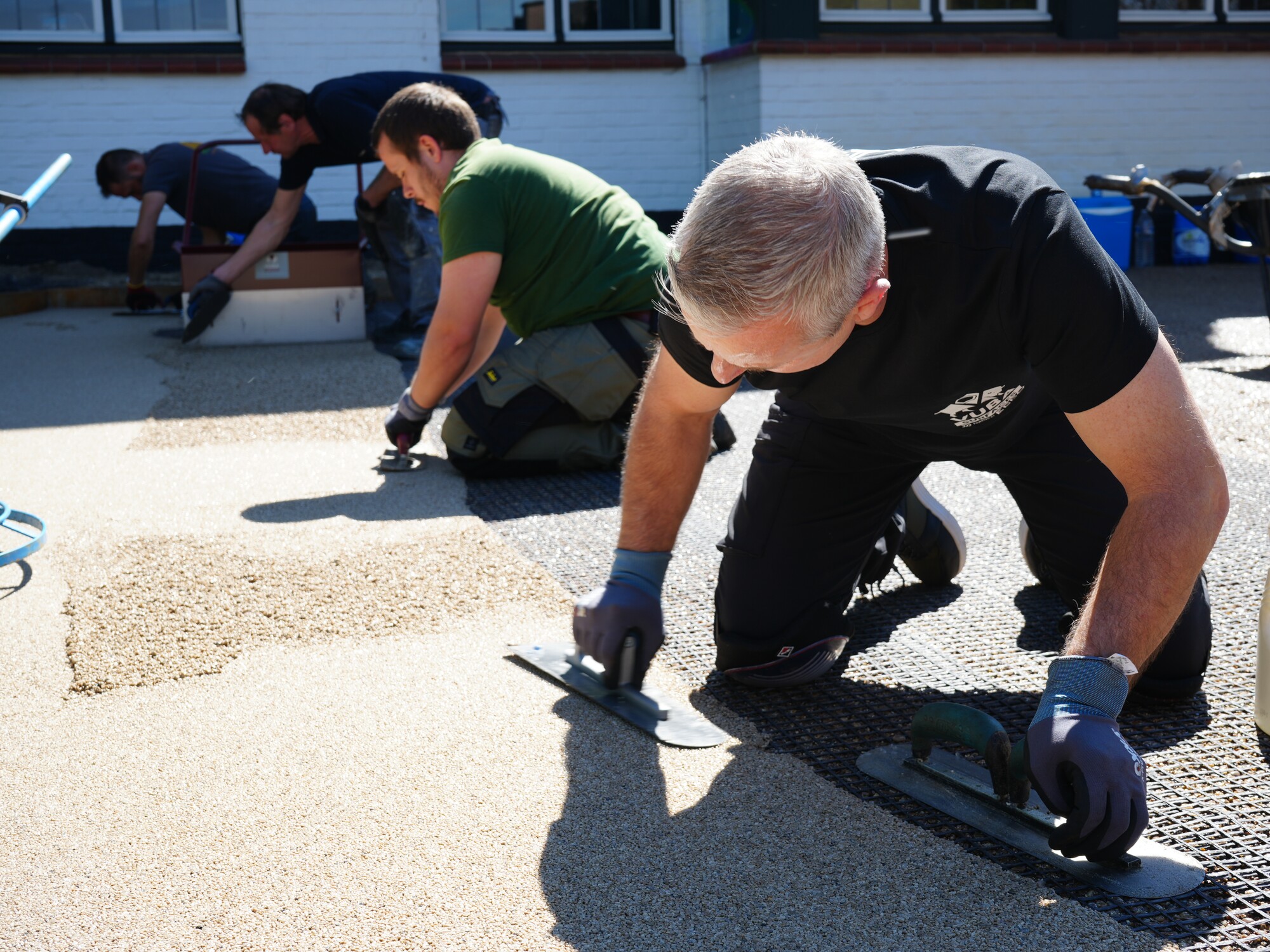 Two people kneeling on pavement, smoothing an asphalt patch outside a building