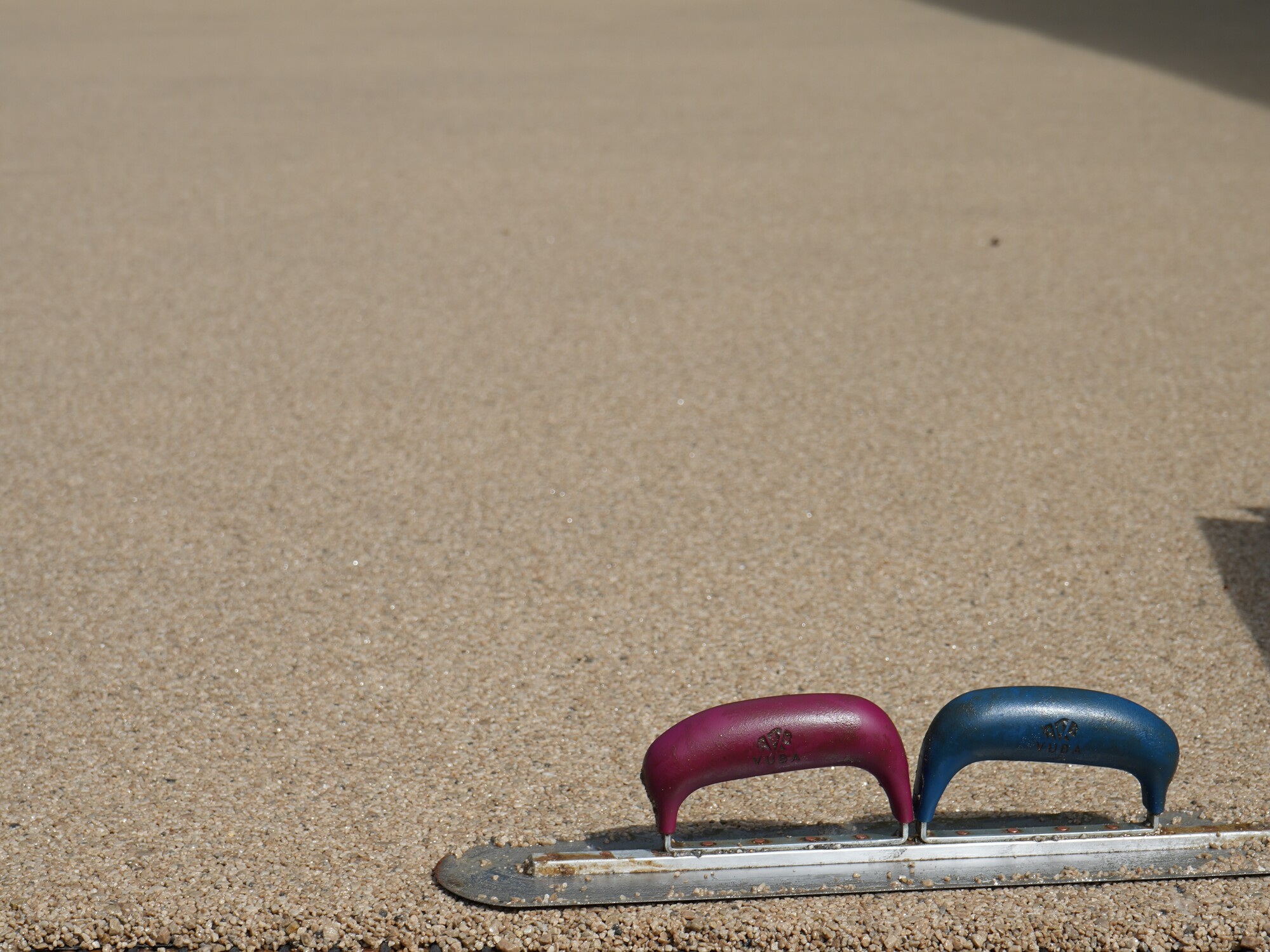 Two small U-shaped handles, pink and blue, on a curb beside textured pavement