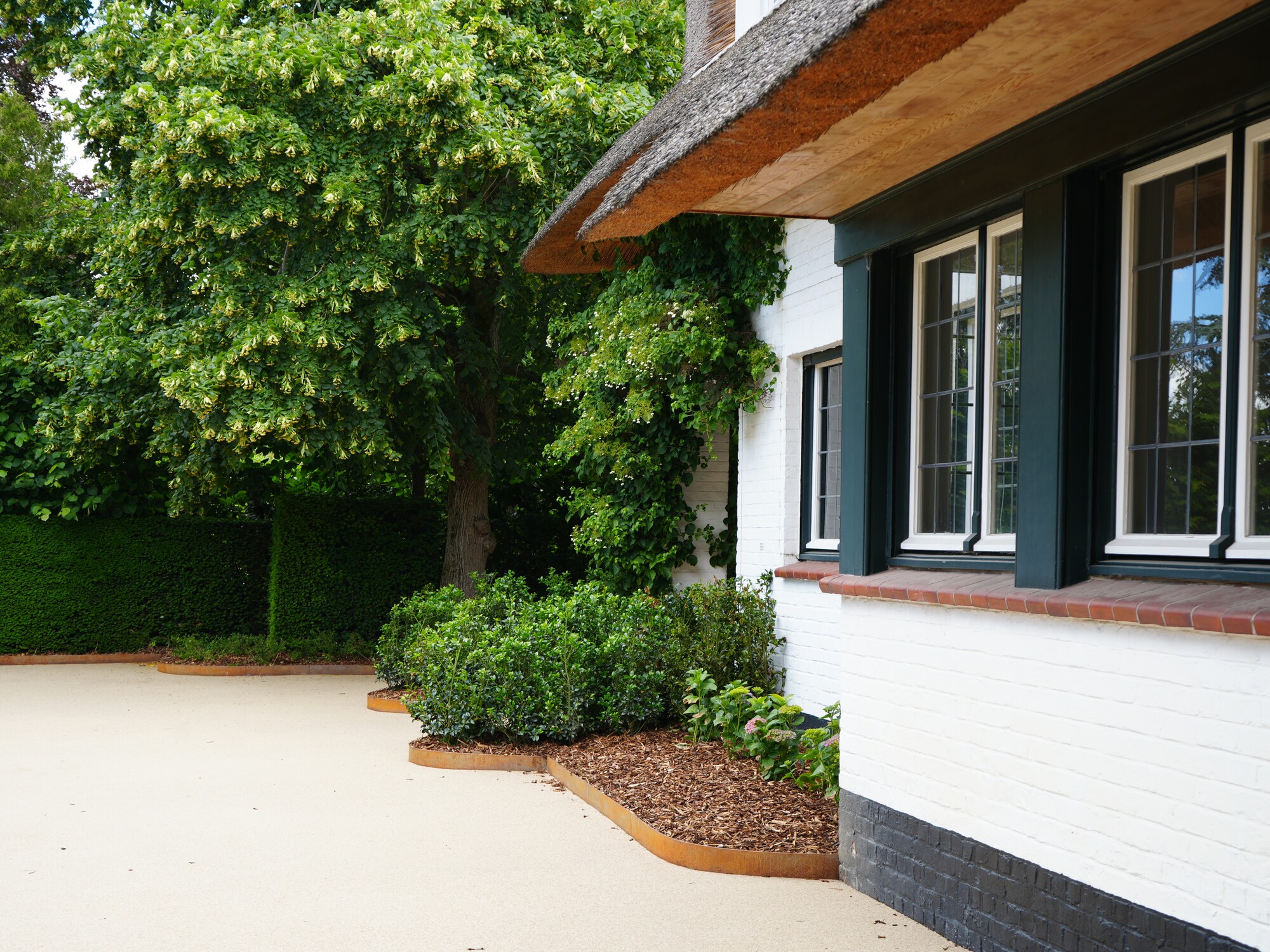 White house with black-framed windows beside a driveway and green trees