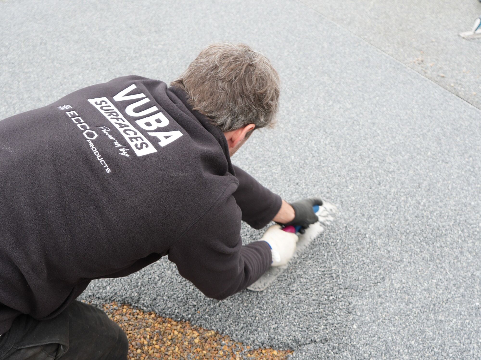 Homme portant un t-shirt NUBA noir, à genoux, travaillant sur une surface asphaltée