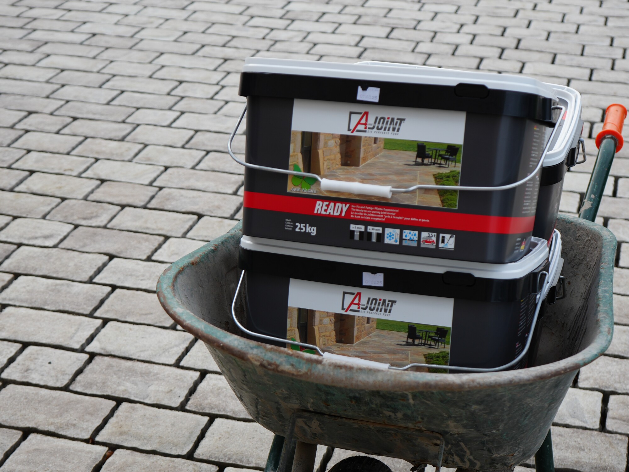 Wheelbarrow carrying two black paint buckets on a brick driveway
