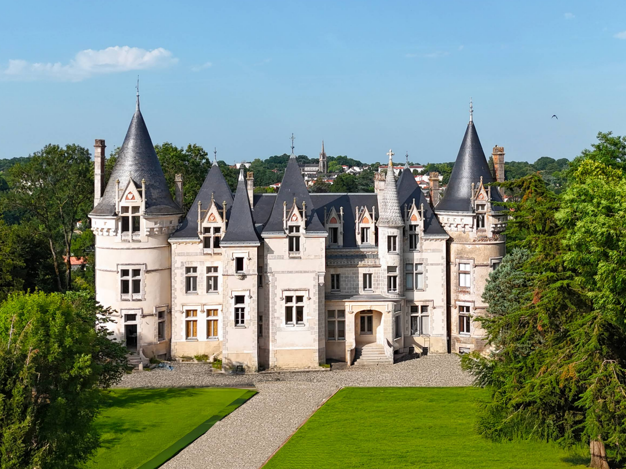 Aerial view of a white castle with turrets amid green lawns and trees under blue sky