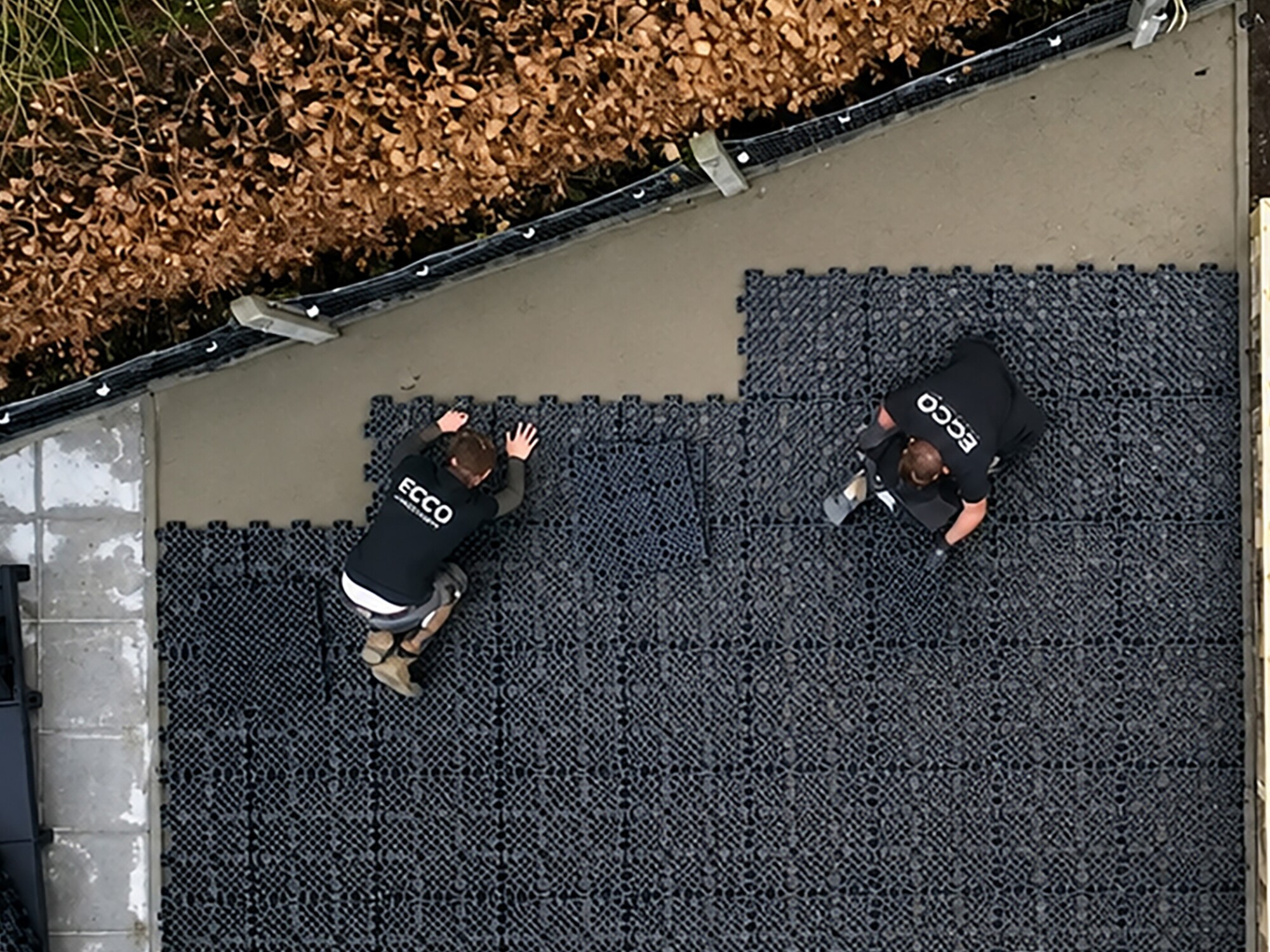 Overhead photo of two workers kneeling on black roofing tiles.
