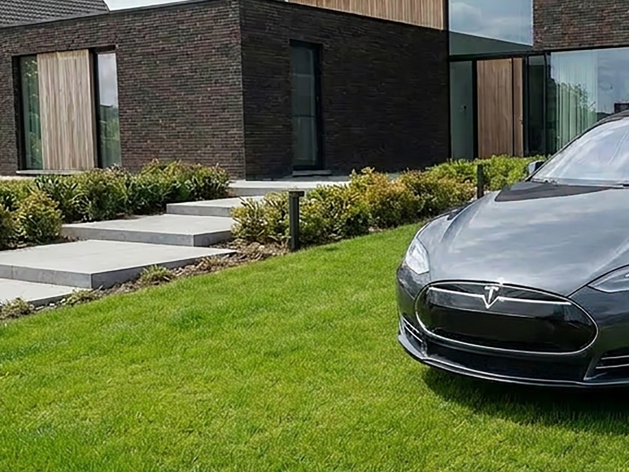 Modern brick house with manicured lawn and a black car parked in the driveway