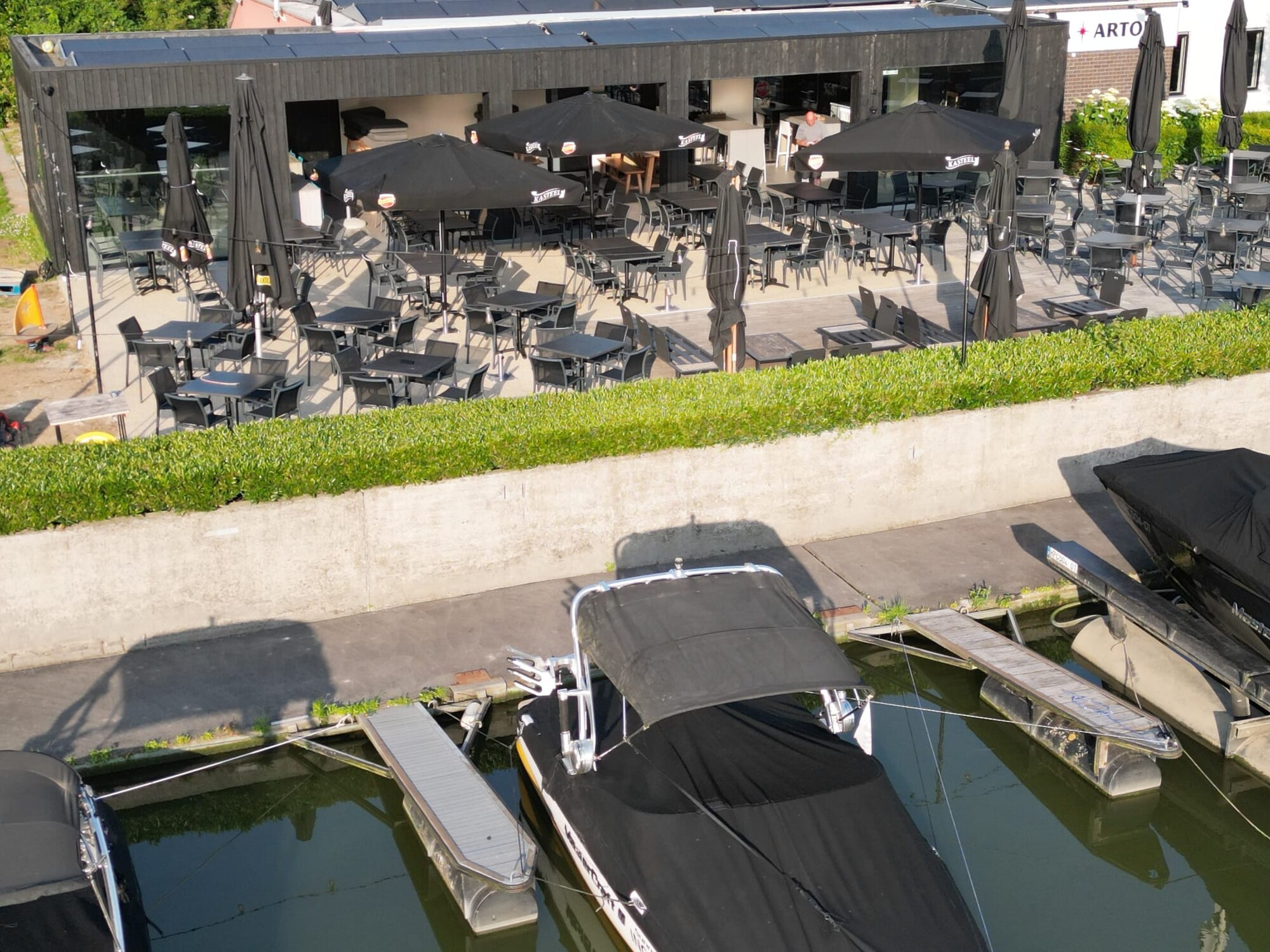 Luftaufnahme von Booten, die an der Außenterrasse eines Restaurants mit Tischen und Stühlen festgemacht sind.