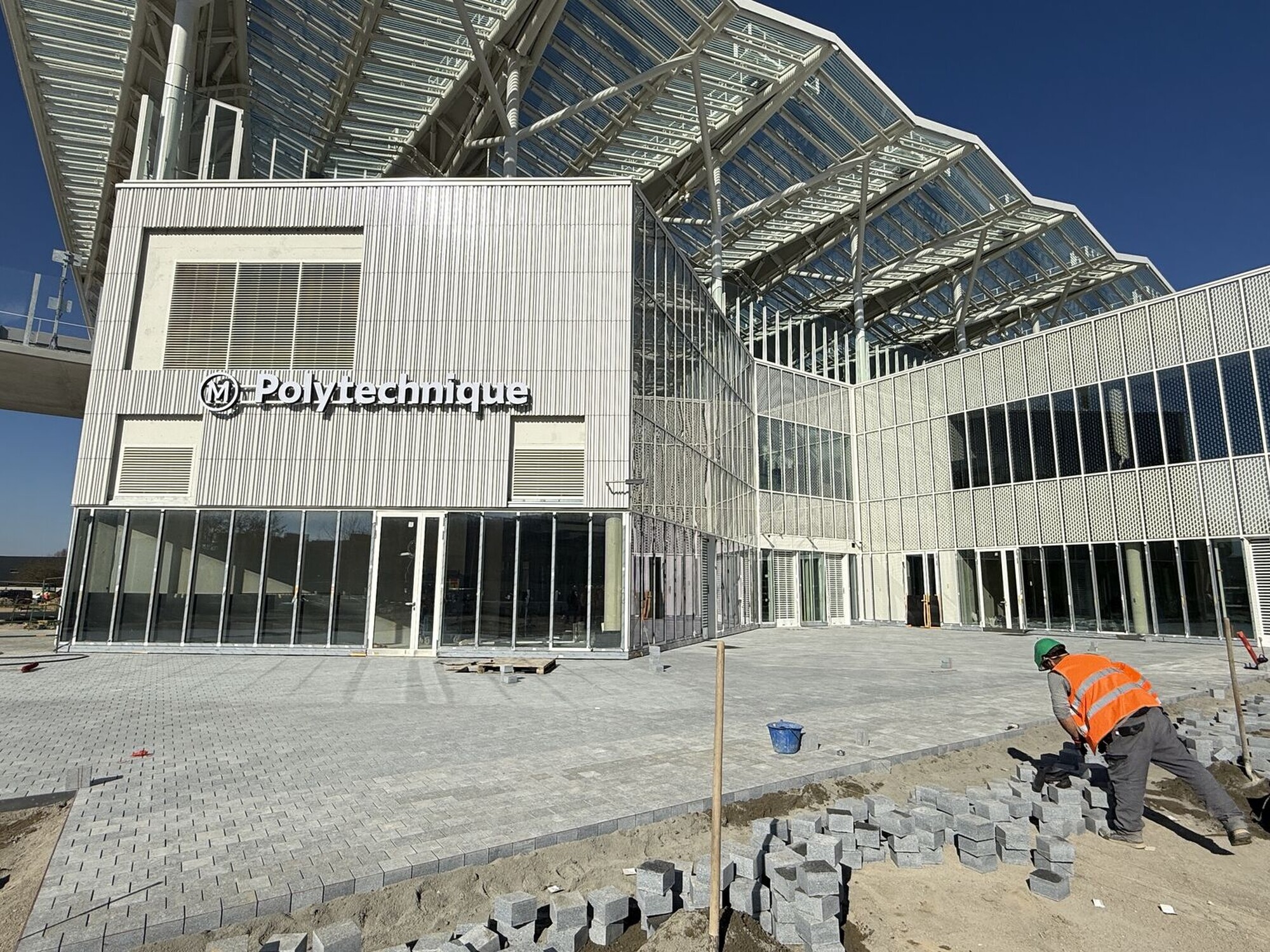 Construction worker in orange vest at a modern building site under clear blue sky