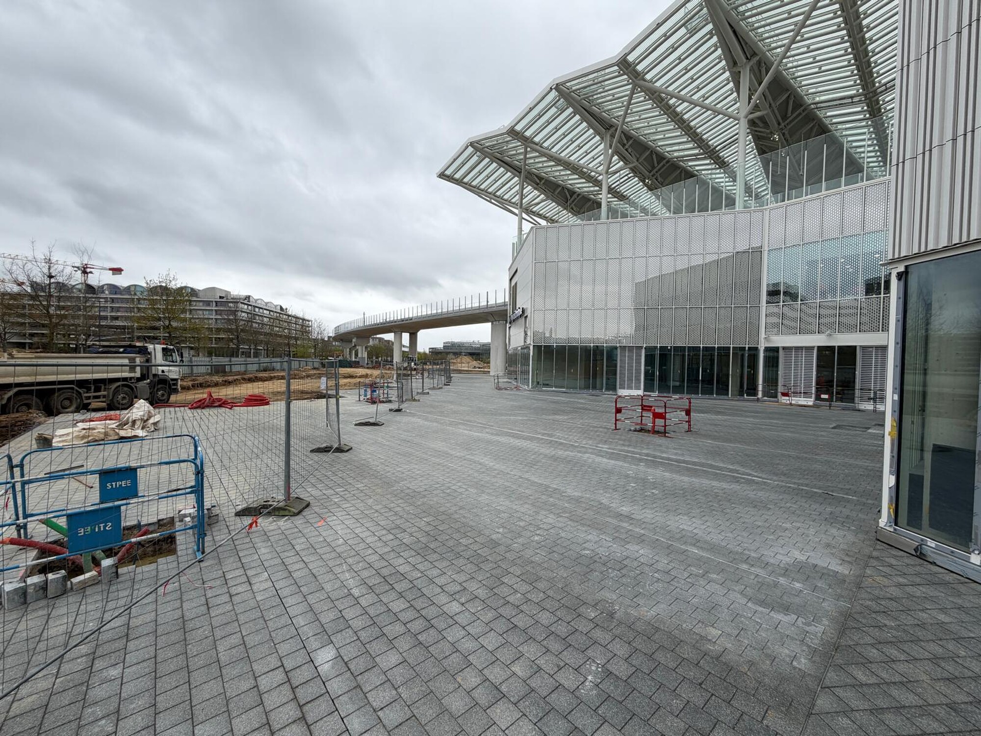Empty paved square outside a modern glass-and-metal building under a cloudy sky