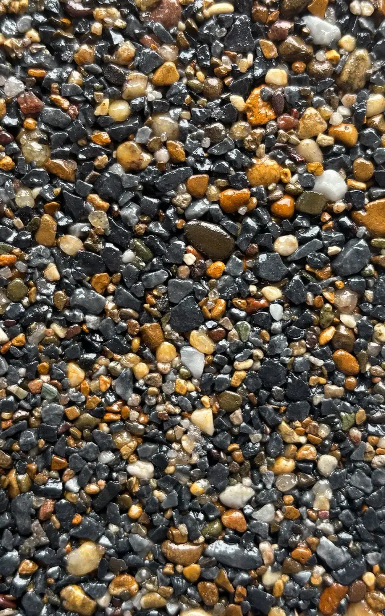 Close-up of dark sand and small pebbles with orange and white stones